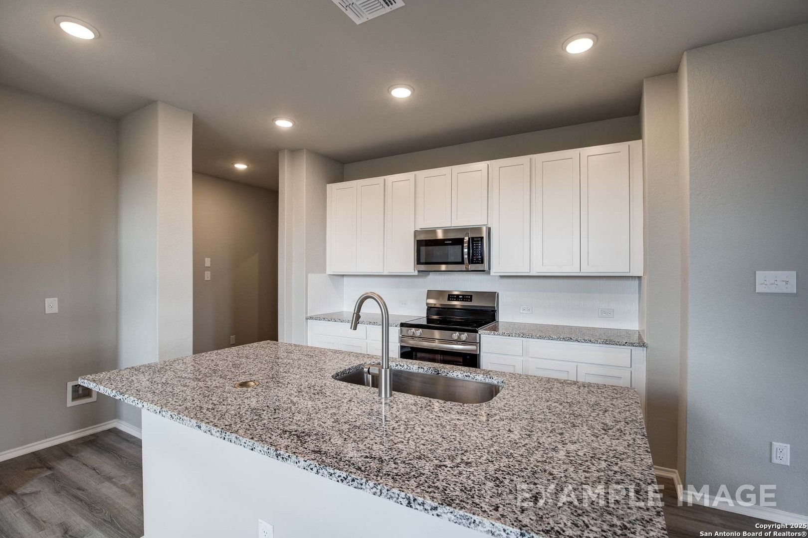 Modern white kitchen with granite island sink, stainless appliances, and open layout in Davidson Homes Blanco C, Agave San Antonio