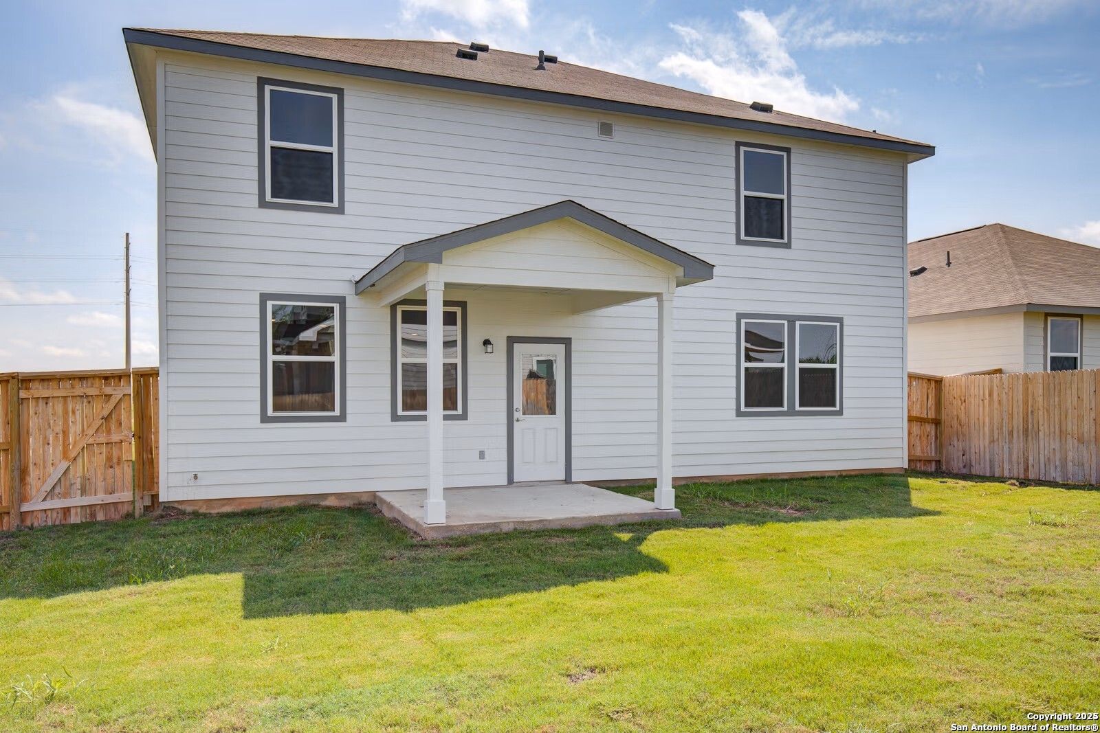 Rear view of two-story Davidson Homes Douglas B with covered patio, large windows, and fenced grassy backyard in Hannah Heights, Seguin, Texas