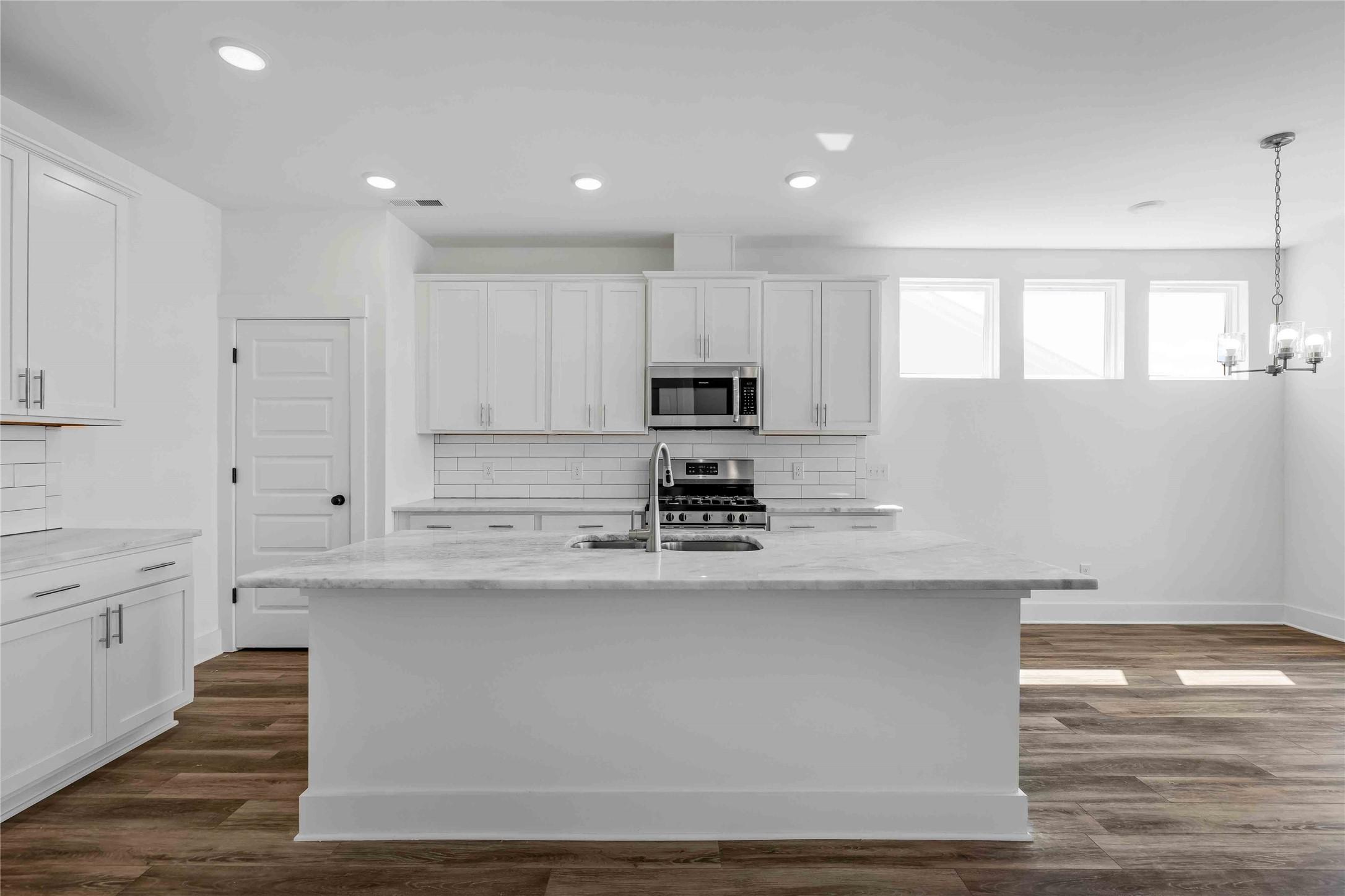 Modern kitchen with white cabinets, marble island, and stainless appliances in The Ash O floor plan by Davidson Homes.