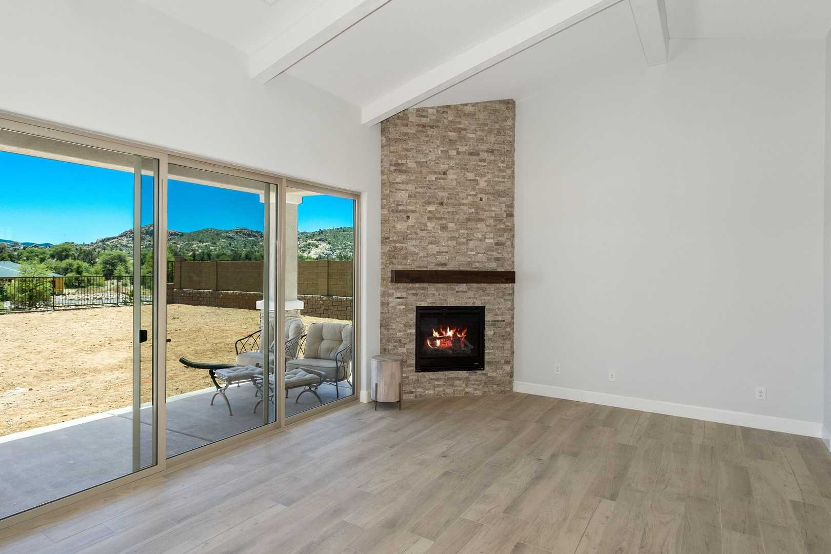 Spacious living room in The Daybreak showcasing brick fireplace, sliding glass doors to Arizona desert views, hardwood floors