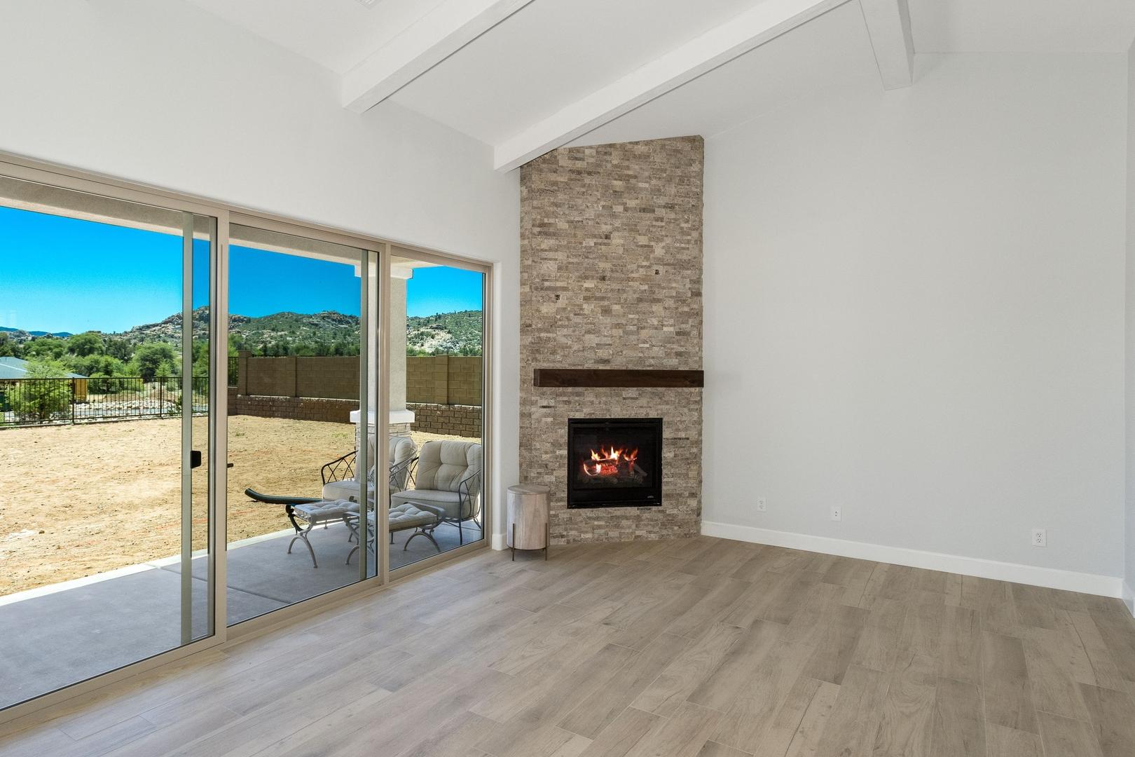 Spacious living room in The Daybreak E with brick fireplace, hardwood floors, and sliding doors to Prescott Arizona desert patio view