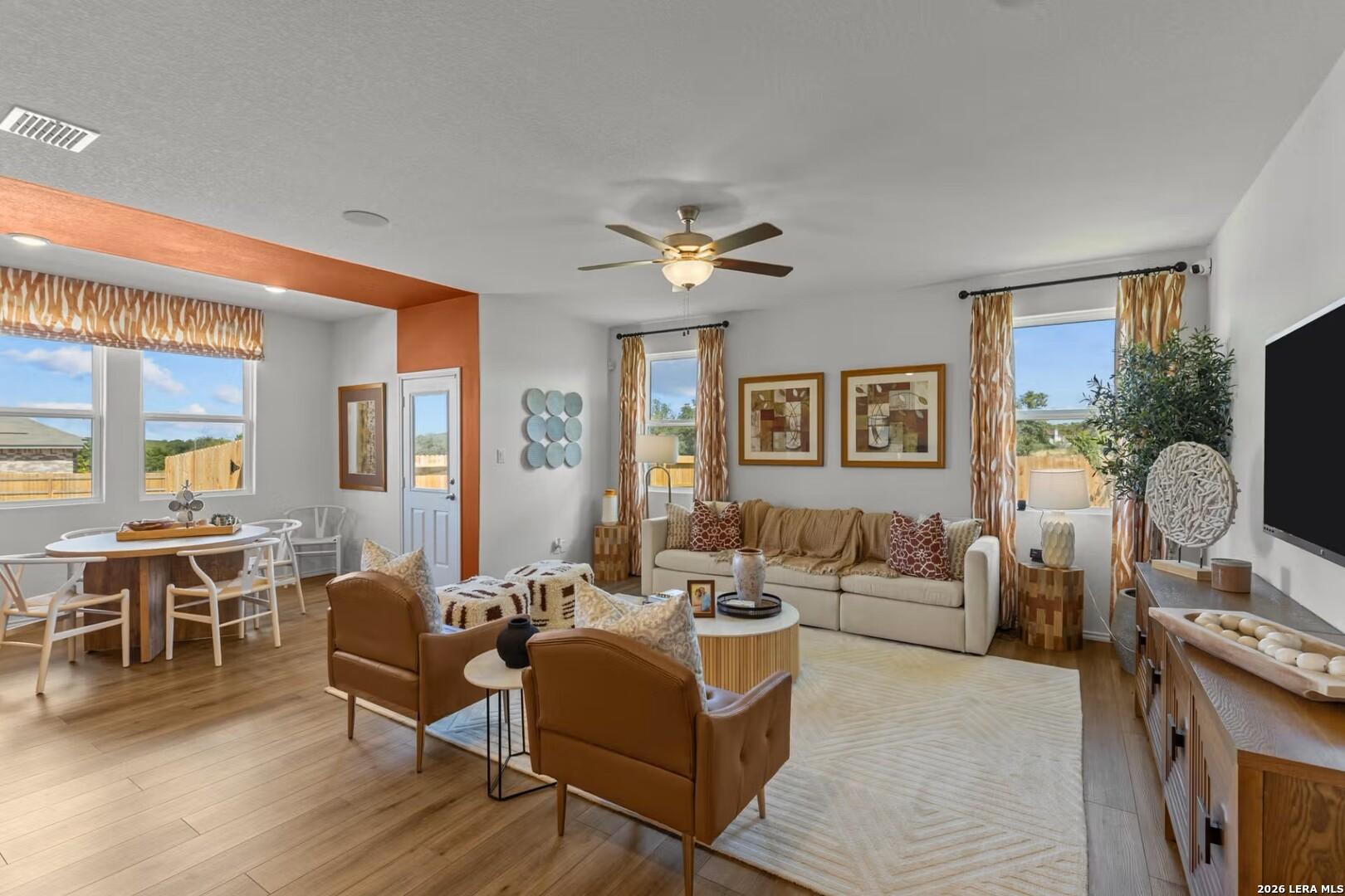 Open living room with beige sectional sofa, leather armchairs, oval dining table, wood floors in The Daphne K home, Bricewood, San Antonio