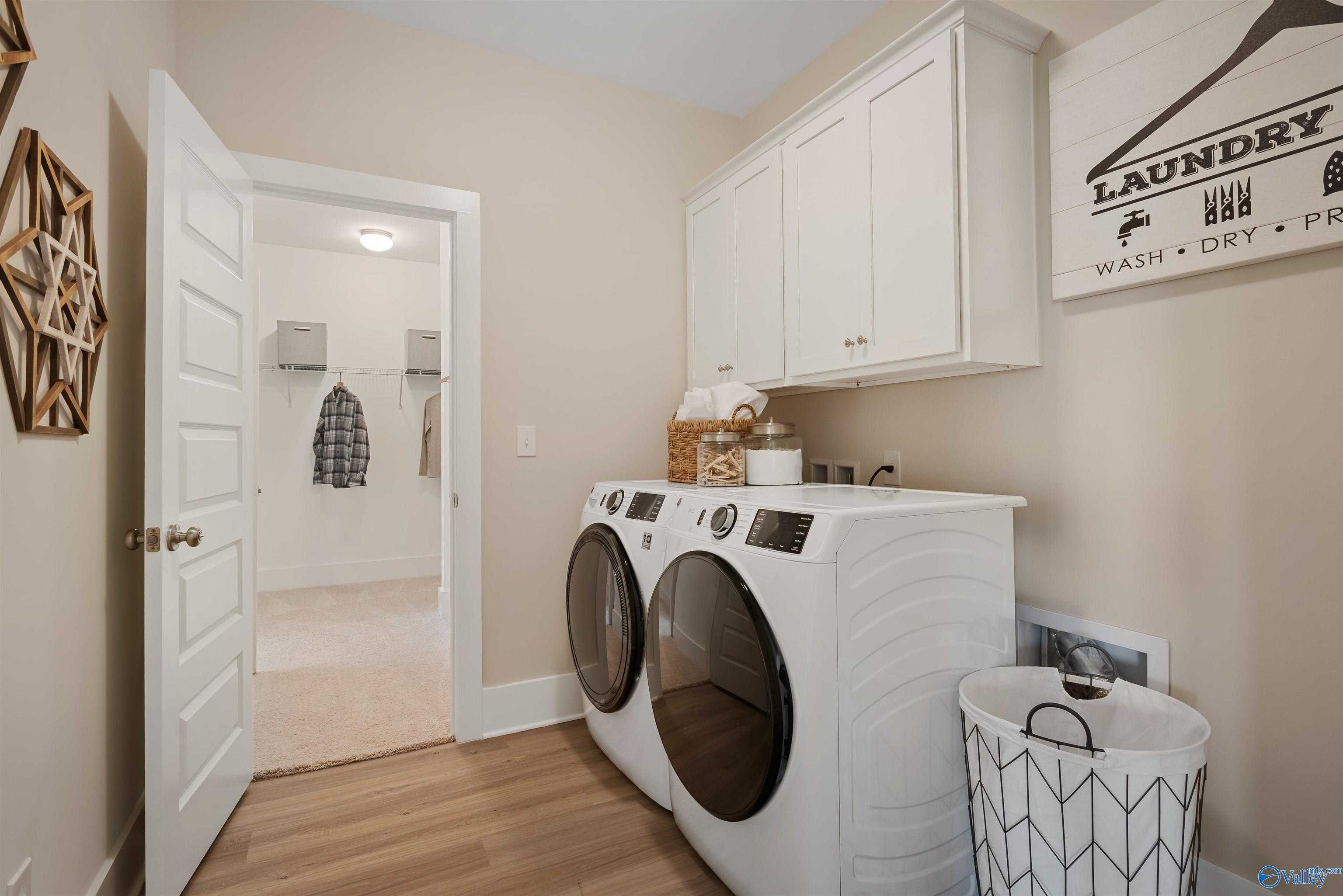 Modern laundry room with white washer-dryer set, cabinets, shelves and basket in Davidson Homes The Everett, New Market, Alabama
