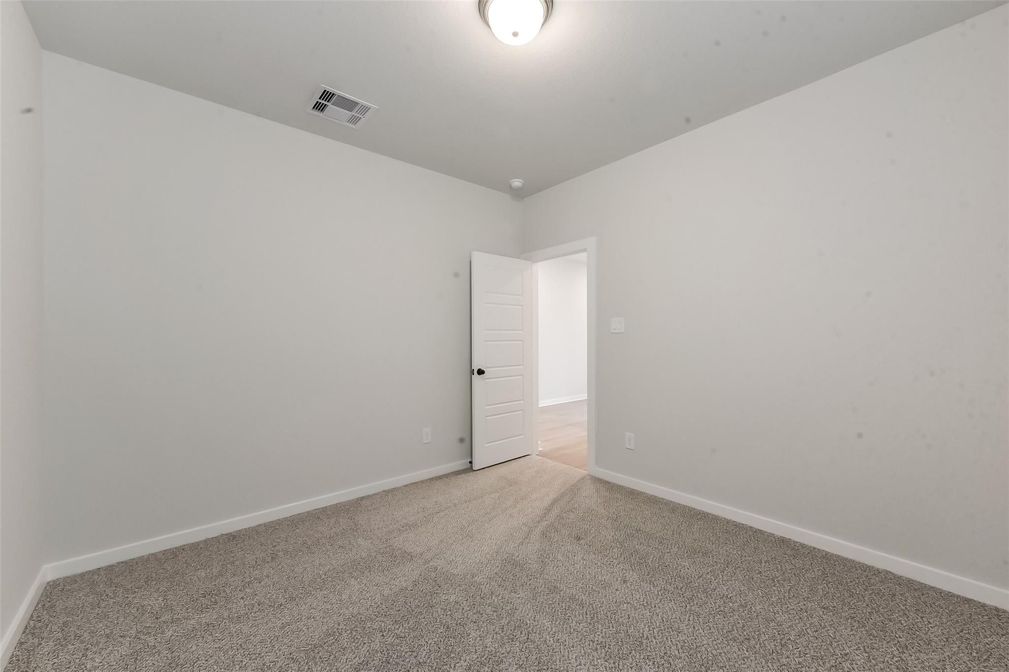Empty bedroom with white walls, beige carpet, open door to hallway in Davidson Homes The Everett C, Sundance Cove, Crosby, Texas