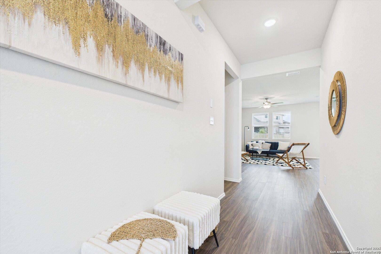 Elegant entry hallway with gold abstract painting, round mirror, and upholstered ottomans in The Asheville K, Bricewood, San Antonio