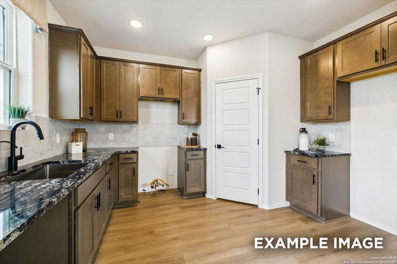 Modern kitchen with dark wood cabinets, granite countertops, stainless sink in Davidson Homes The Florence C, San Antonio, Texas