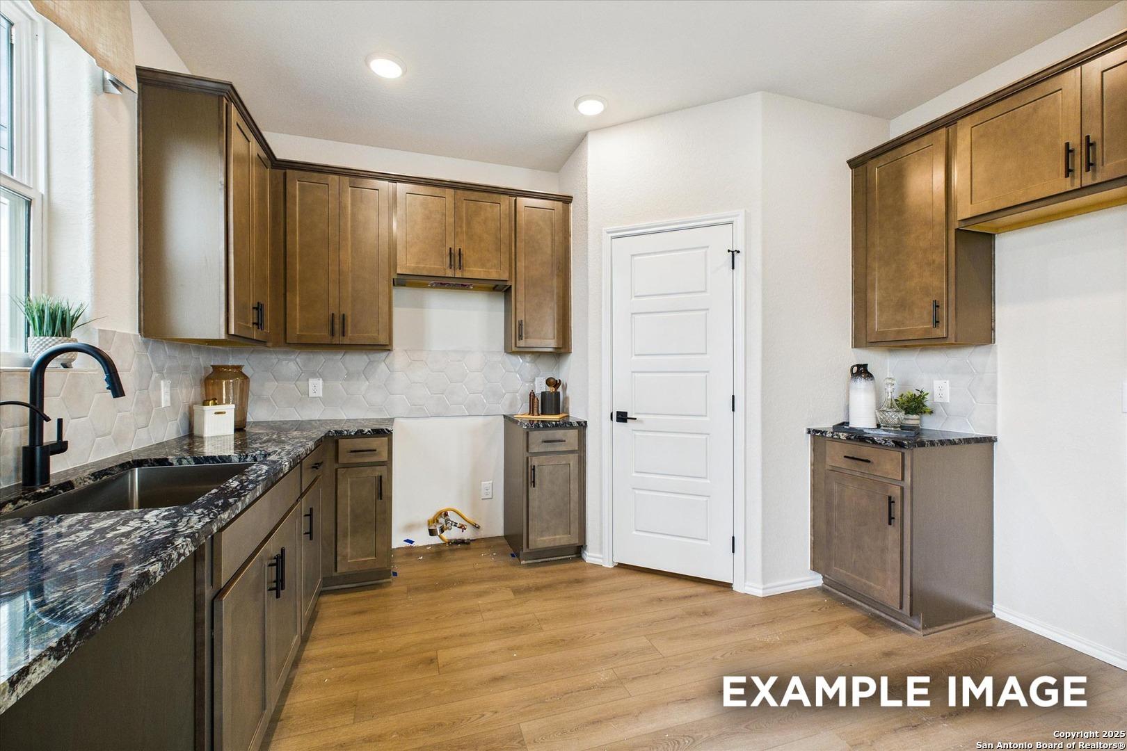 Modern kitchen with dark wood cabinets, granite countertops, stainless sink in Davidson Homes The Florence C, San Antonio, Texas