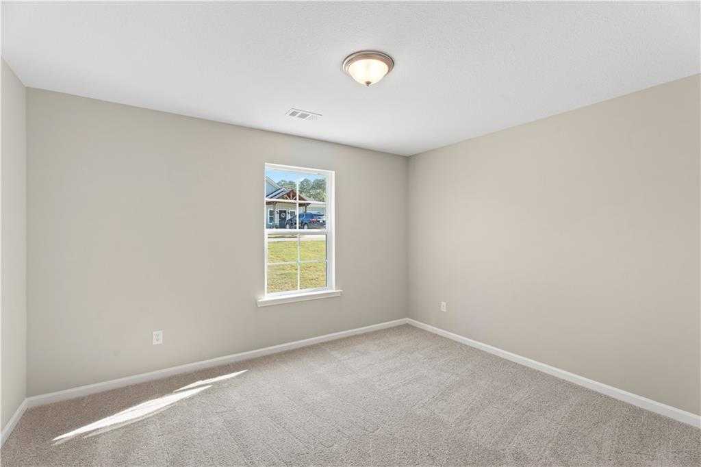 Cozy secondary bedroom with beige walls, plush carpet, and large window overlooking neighborhood in Davidson Homes The Washington, Phenix City, Alabama