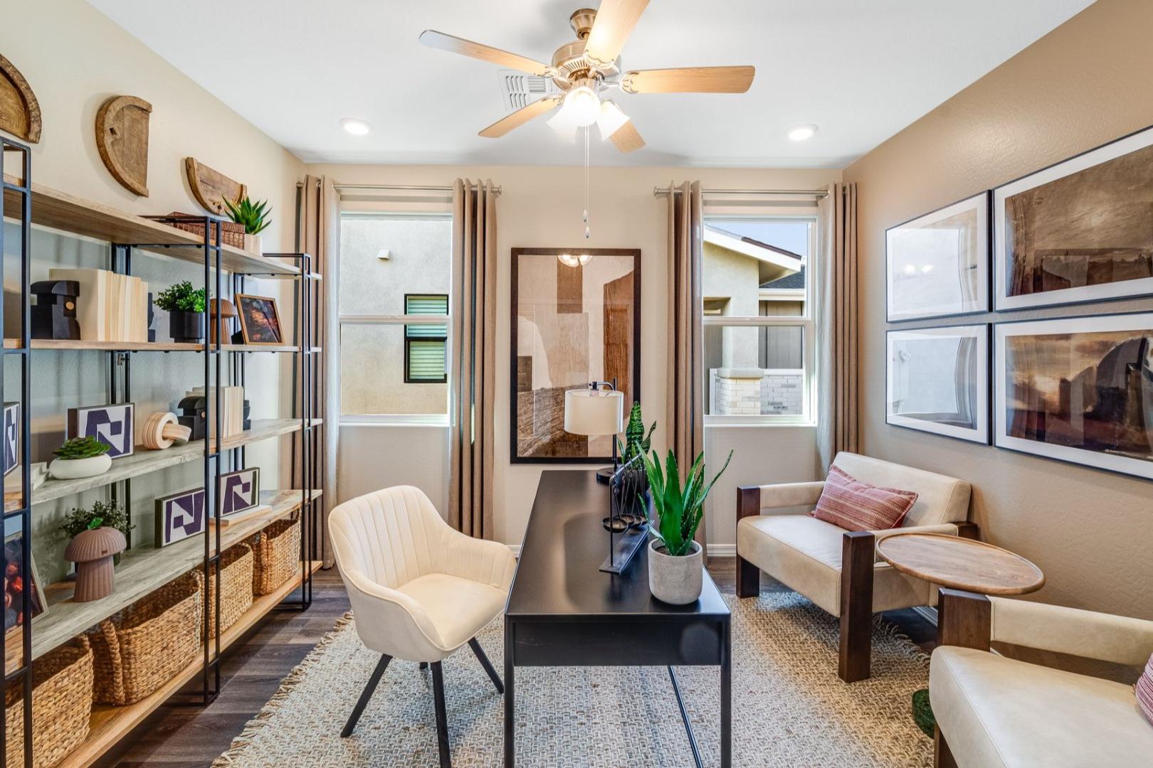 Cozy home office in The Savannah B showcasing bookshelves, white leather chairs, black desk, plants, and large windows