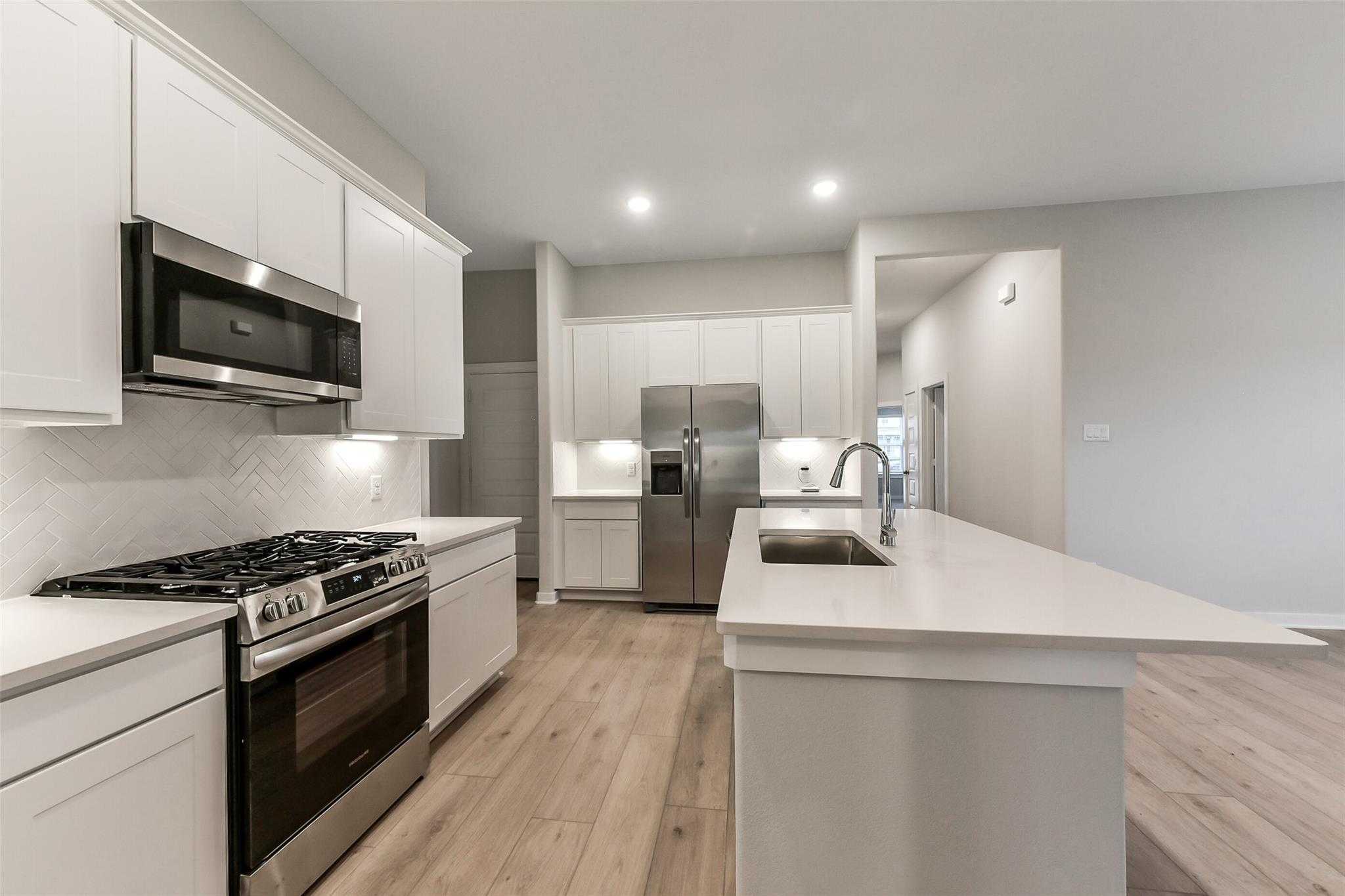 Modern white kitchen with stainless steel appliances, gas range, and spacious island in Davidson Homes The Laguna B, Katy, Texas