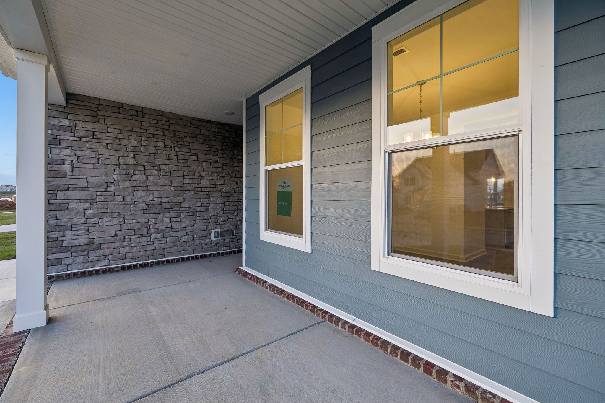 Covered front porch with stone accent wall and blue siding on Davidson Homes The Willow A in Calista Farms, White House, Tennessee