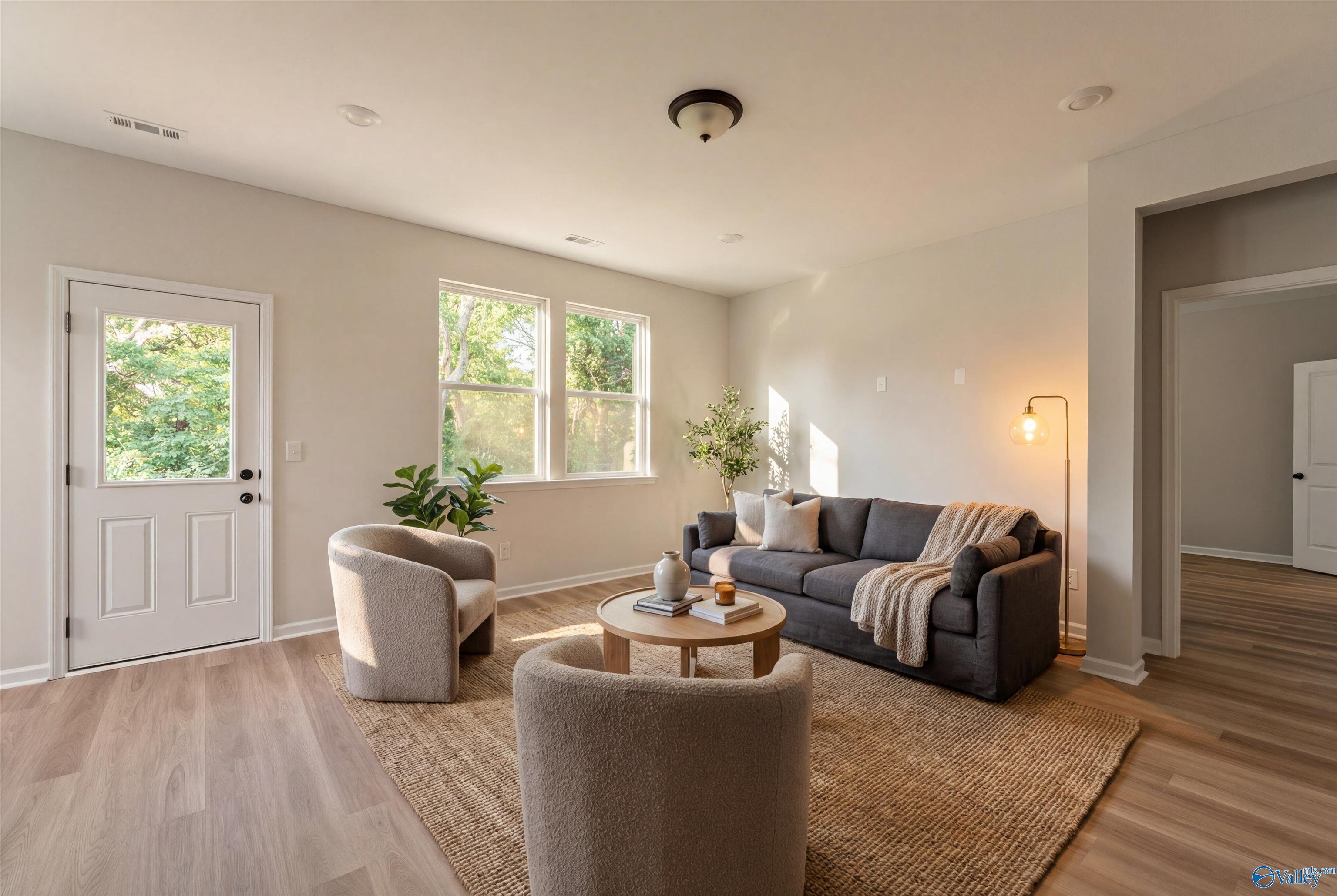 Cozy living room with gray sofa, cream armchairs, wooden coffee table, and large windows in Davidson Homes The Phoenix, Hazel Green, Alabama