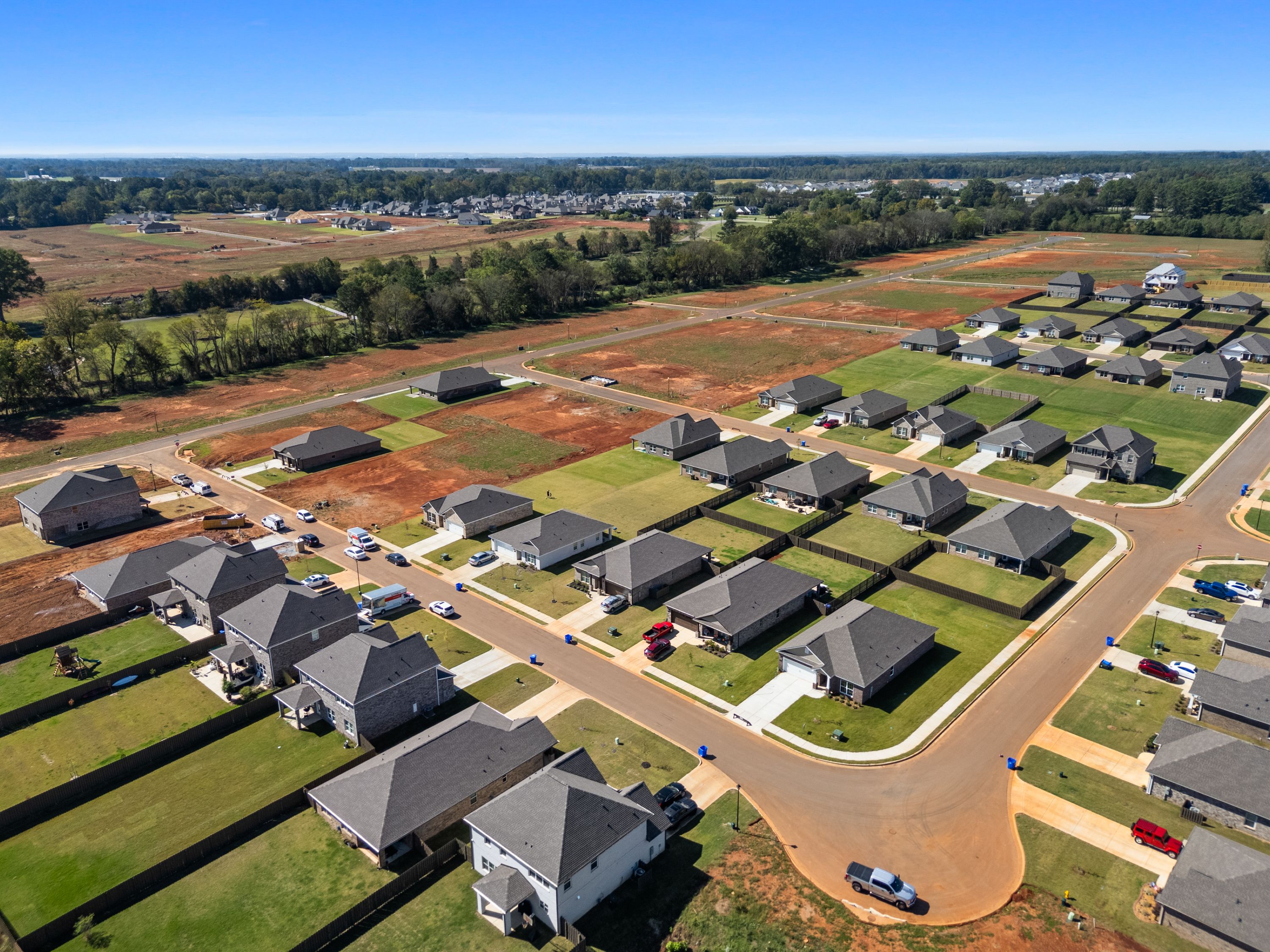 Aerial view of new homes in The Meadows, Athens Alabama, with gray roofs, paved streets, and red dirt construction sites