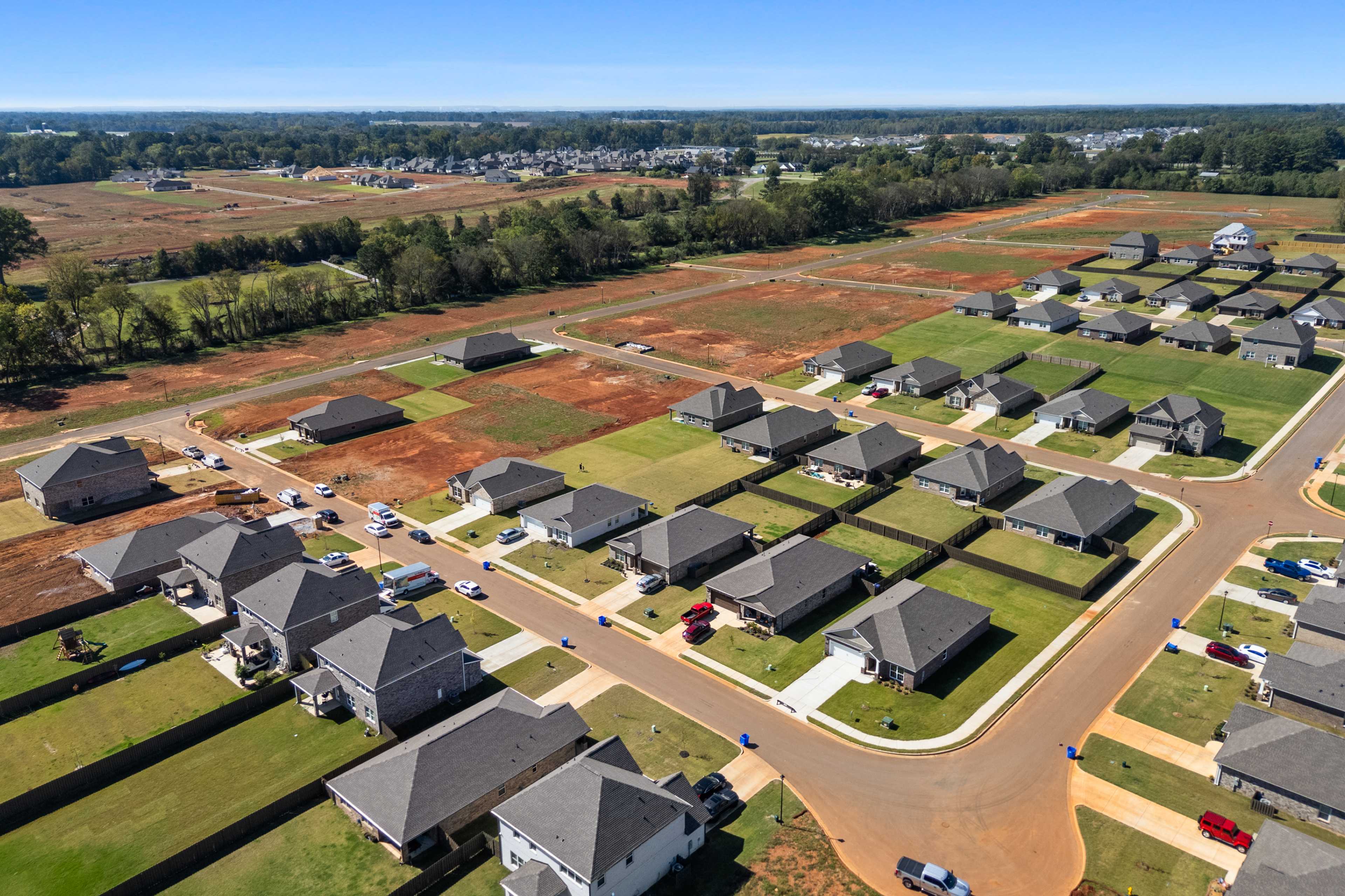 Aerial view of new homes in The Meadows, Athens Alabama, with gray roofs, paved streets, and red dirt construction sites