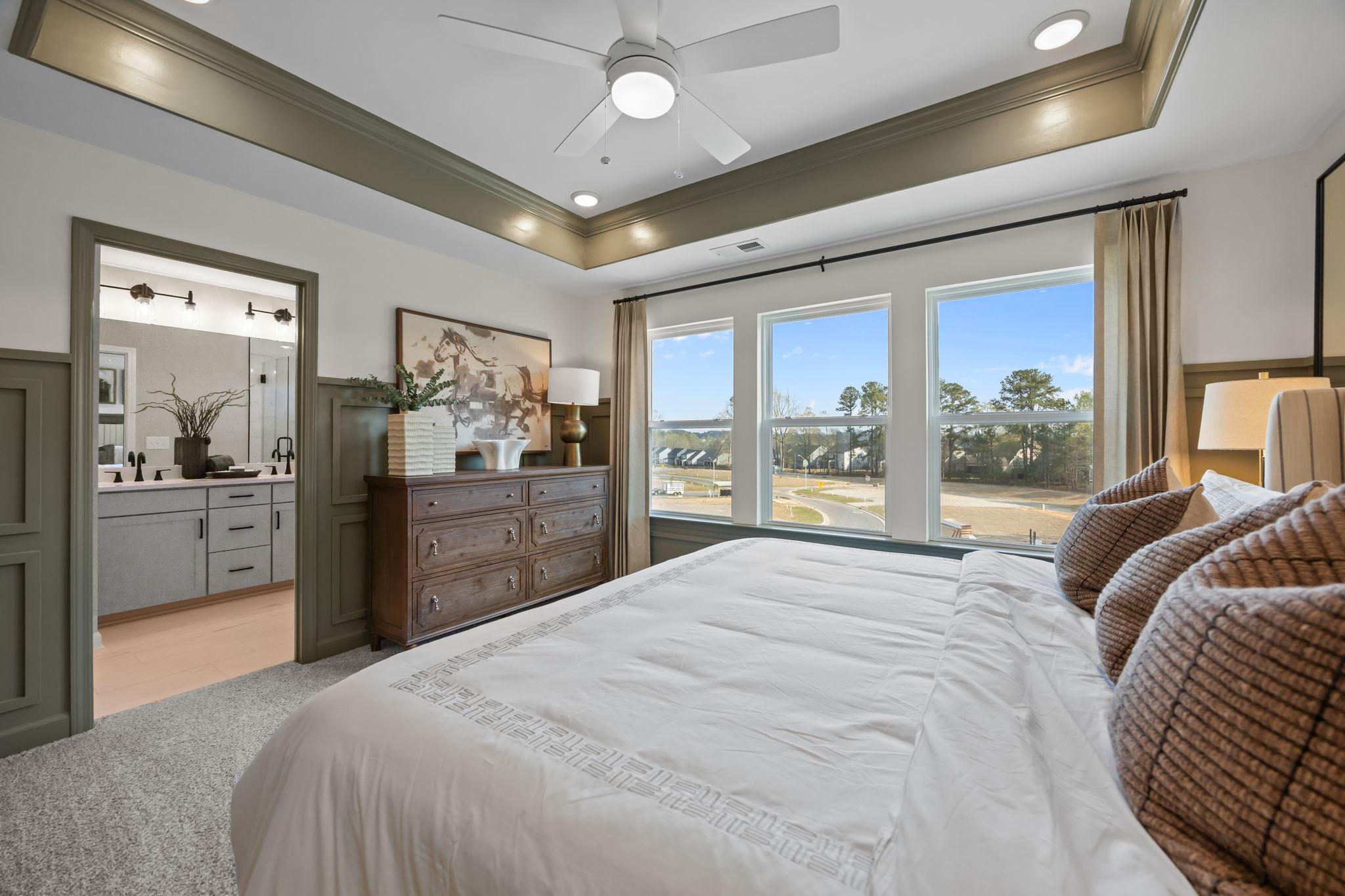 Spacious primary bedroom at Camden Park in Knightdale NC featuring king bed, wooden dresser, ceiling fan, and pond-view windows