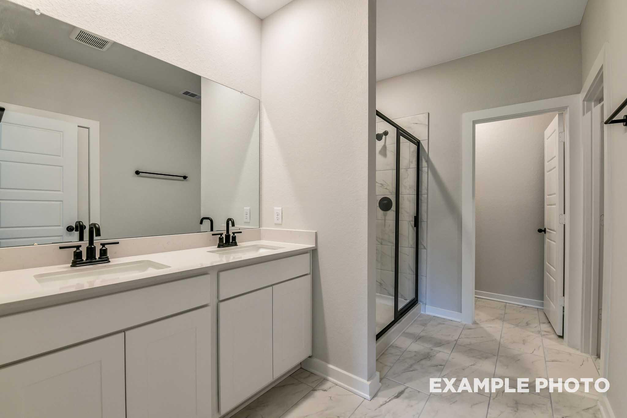 Master bathroom in The Daphne G with double vanity, black faucets, large mirror, and glass shower enclosure