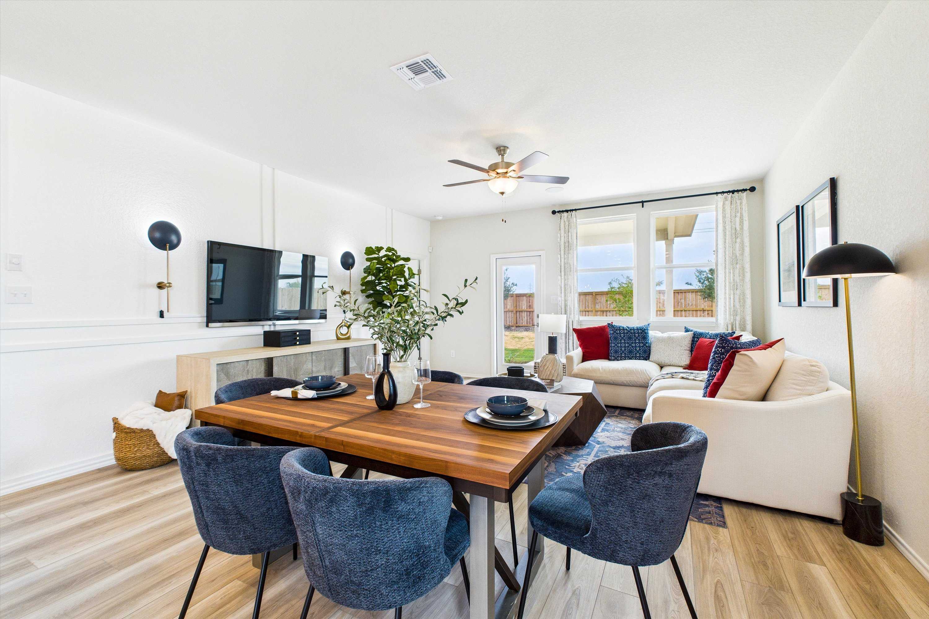 Open-concept dining and living area in Agave San Antonio TX by Davidson Homes with wooden table, blue chairs, white sofa, and large windows