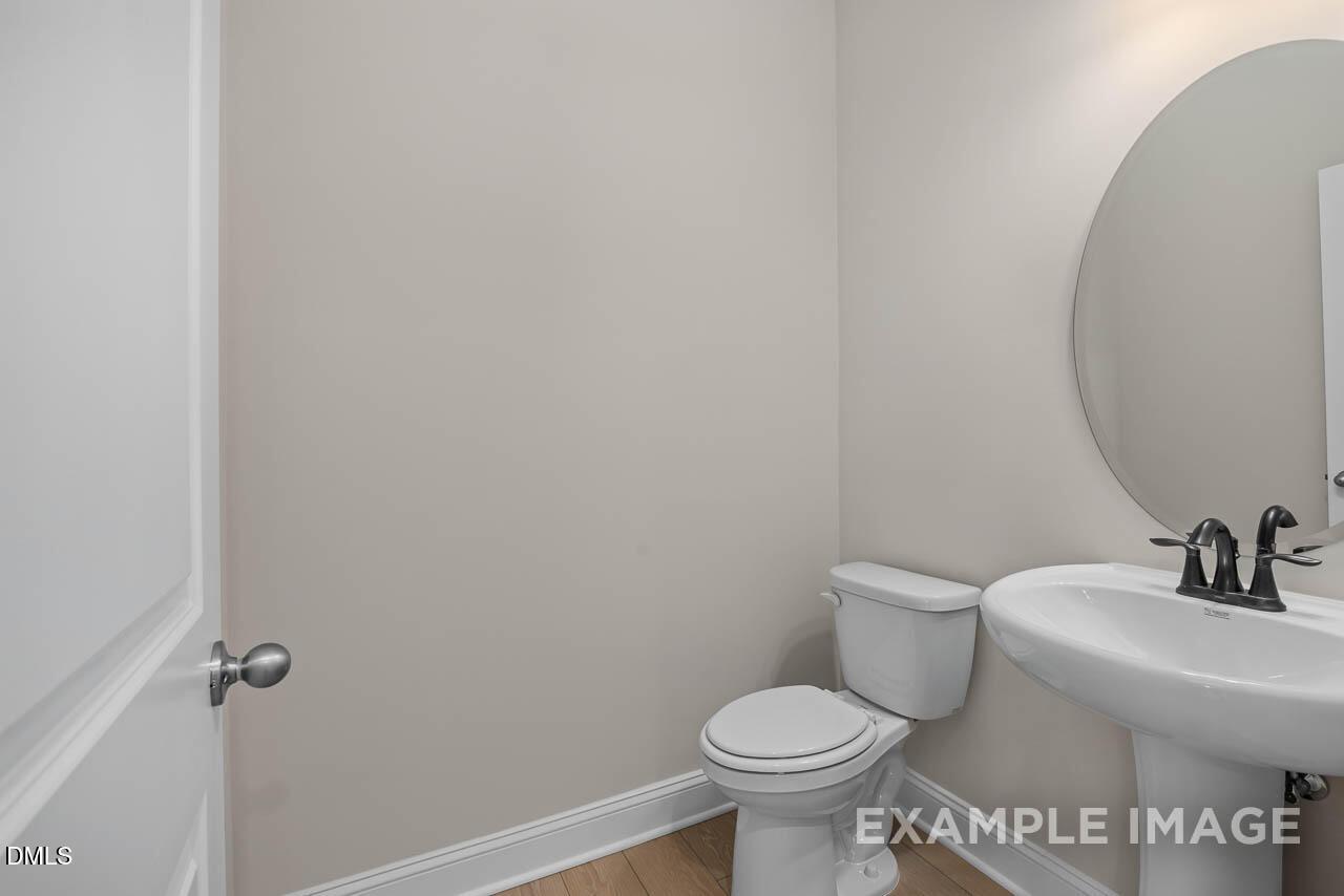Elegant powder room with white sink, toilet, and round mirror in Davidson Homes The Crawford D, Angier, North Carolina