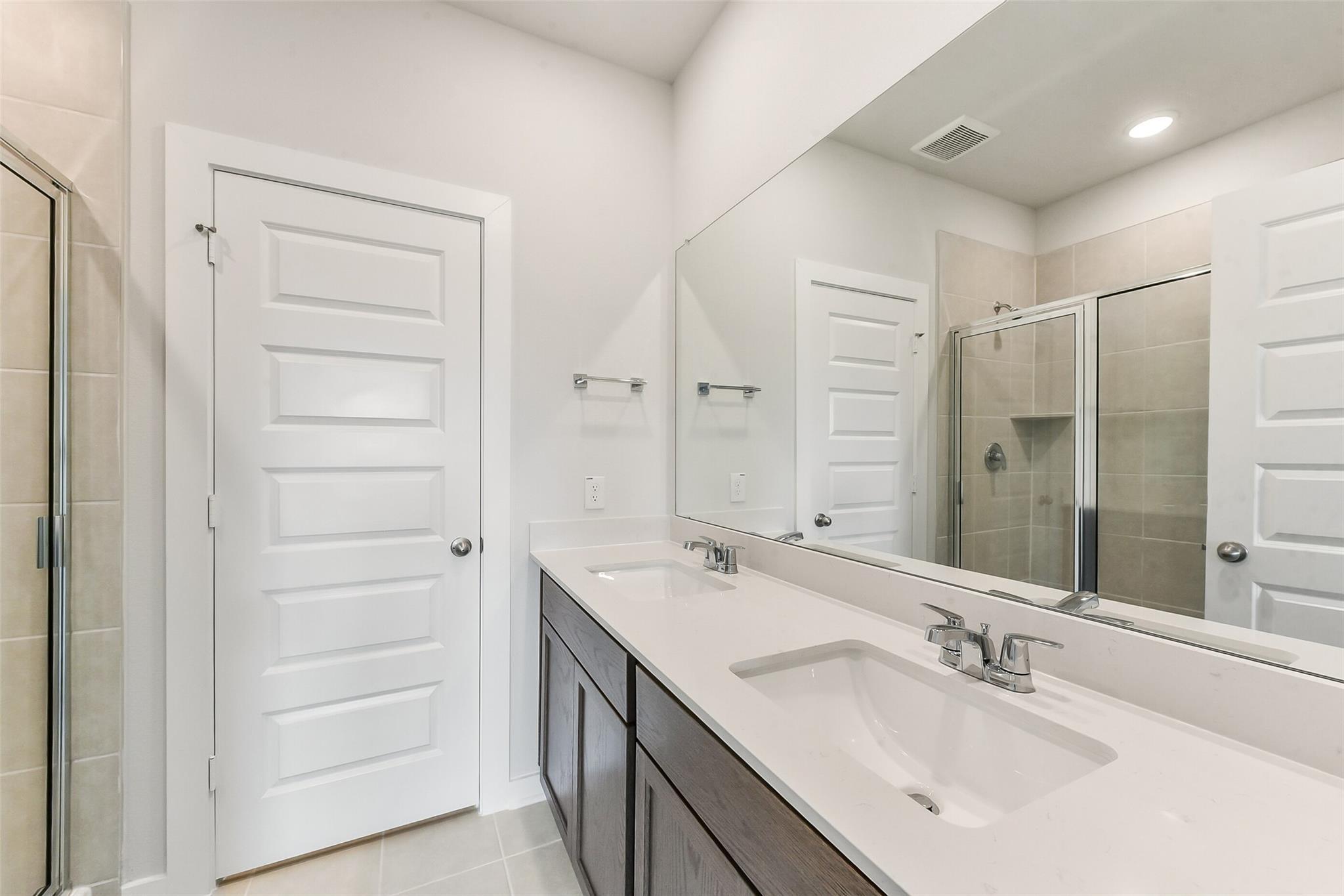 Modern double vanity with quartz countertop, dark cabinets, and glass shower in Davidson Homes The Sabine F, Dayton, Texas