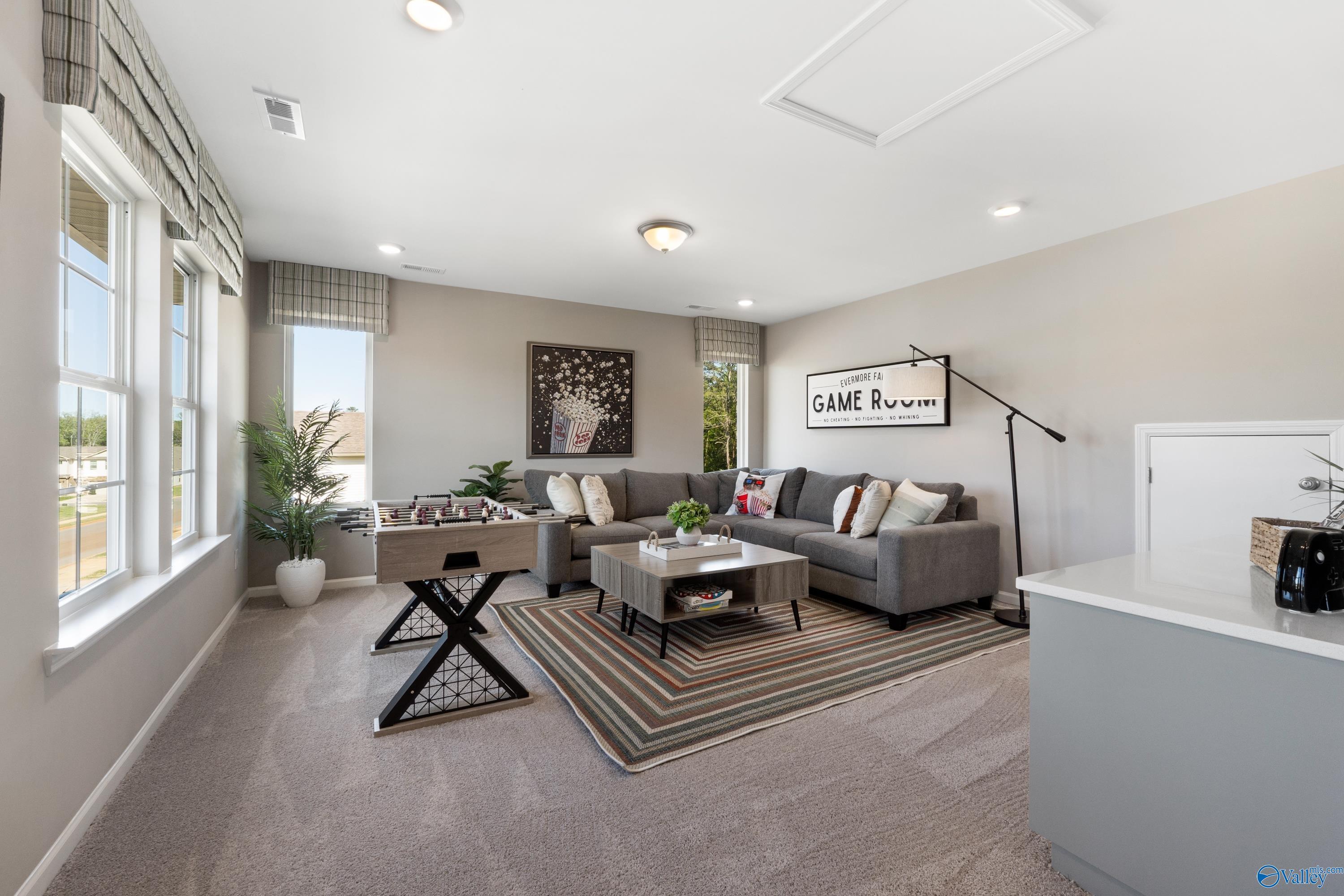 Cozy game room with gray sectional sofa, foosball table, and entertainment sign in Davidson Homes The Stella, Madison, Alabama