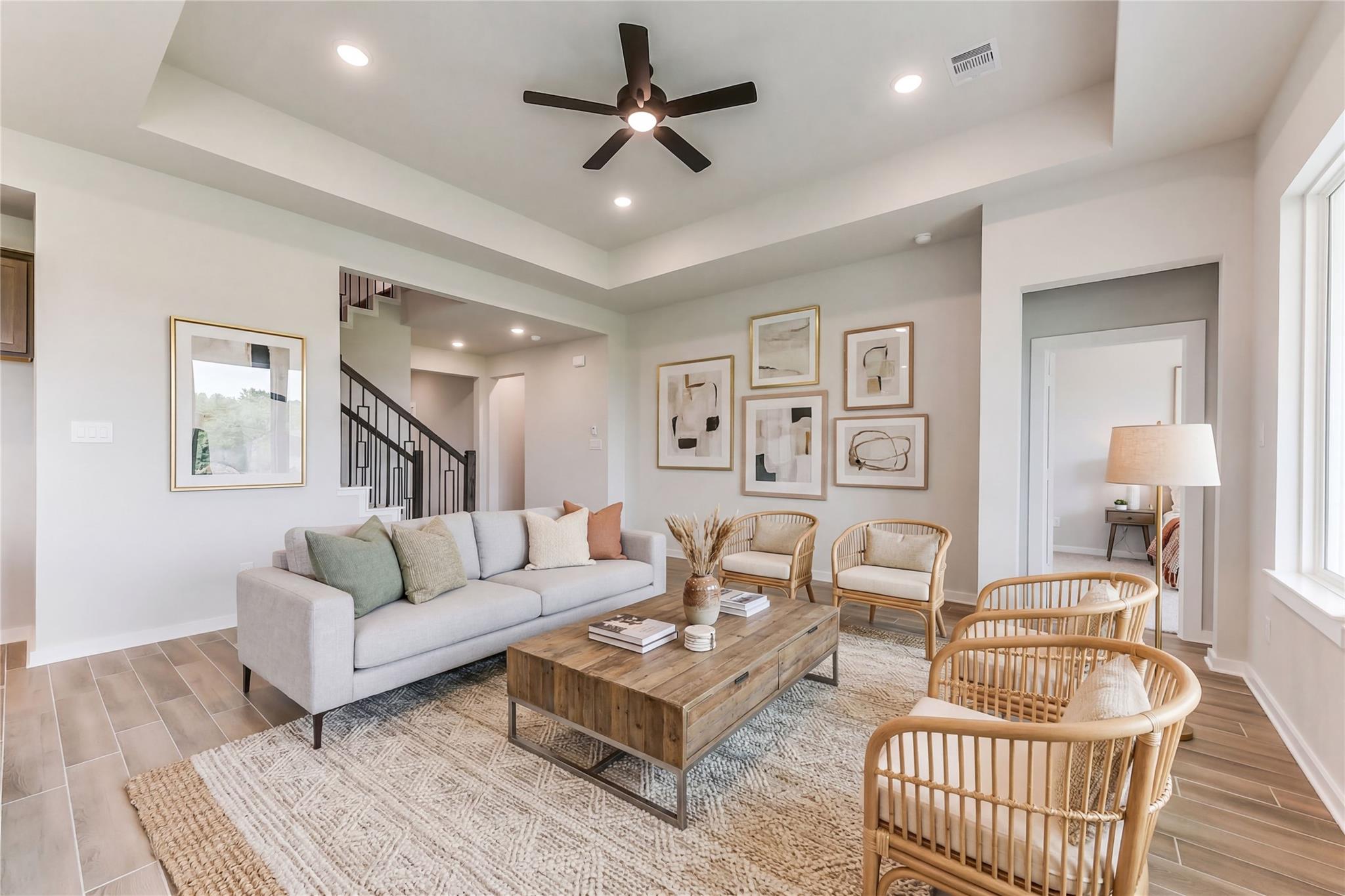 Cozy living room with gray sofa, rattan chairs, wooden coffee table, abstract art, and open staircase in Davidson Homes The Sequoia C, Crosby, Texas