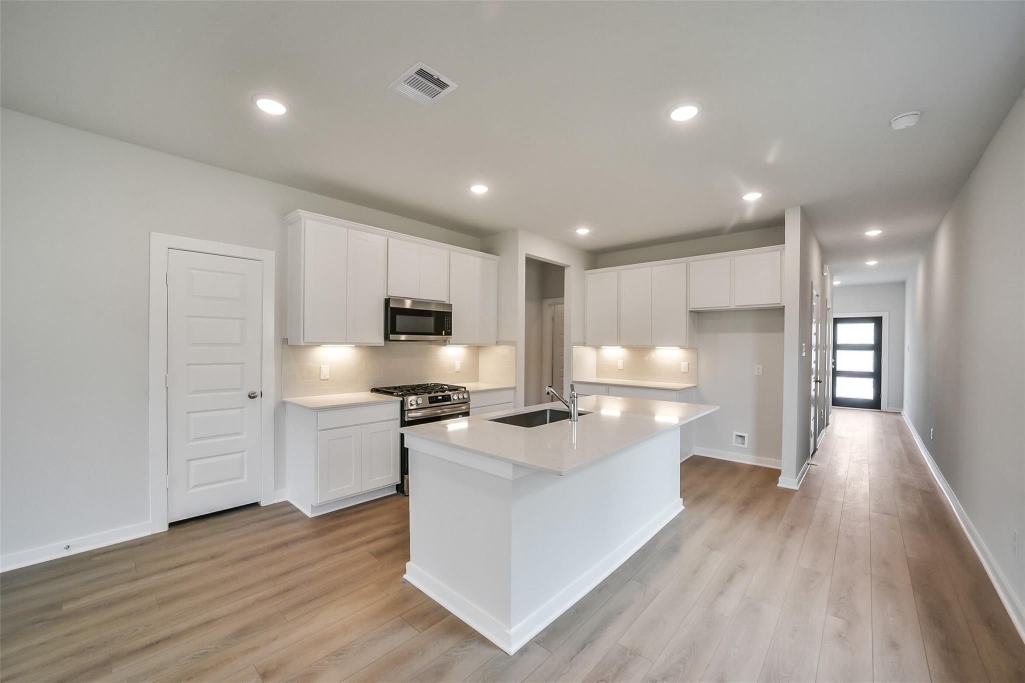 Bright modern kitchen with white cabinets, large island sink, stainless appliances, open to hallway in Davidson Homes The Frio F, Conroe Texas