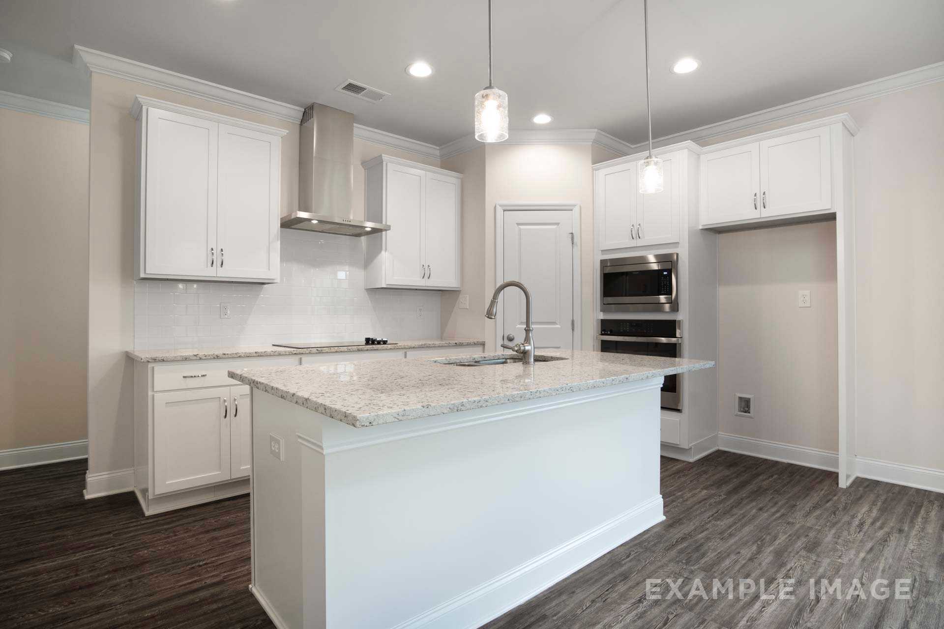 Modern kitchen in The Charleston with white shaker cabinets, granite center island, double wall ovens, and pendant lights