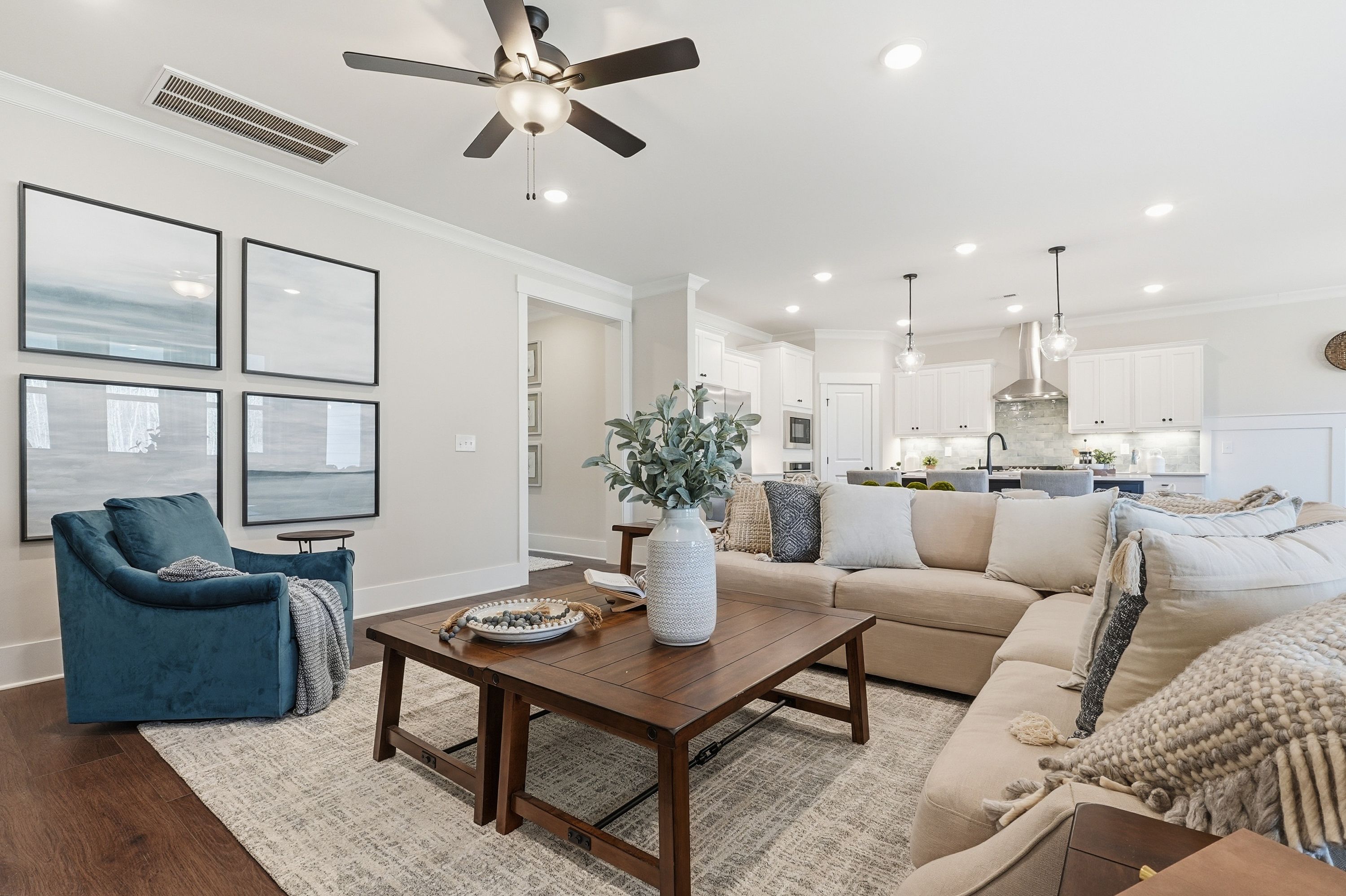 Cozy open-concept living room in Noble Ridge Cullman Alabama with blue velvet armchair beige sofa wooden coffee table and white kitchen