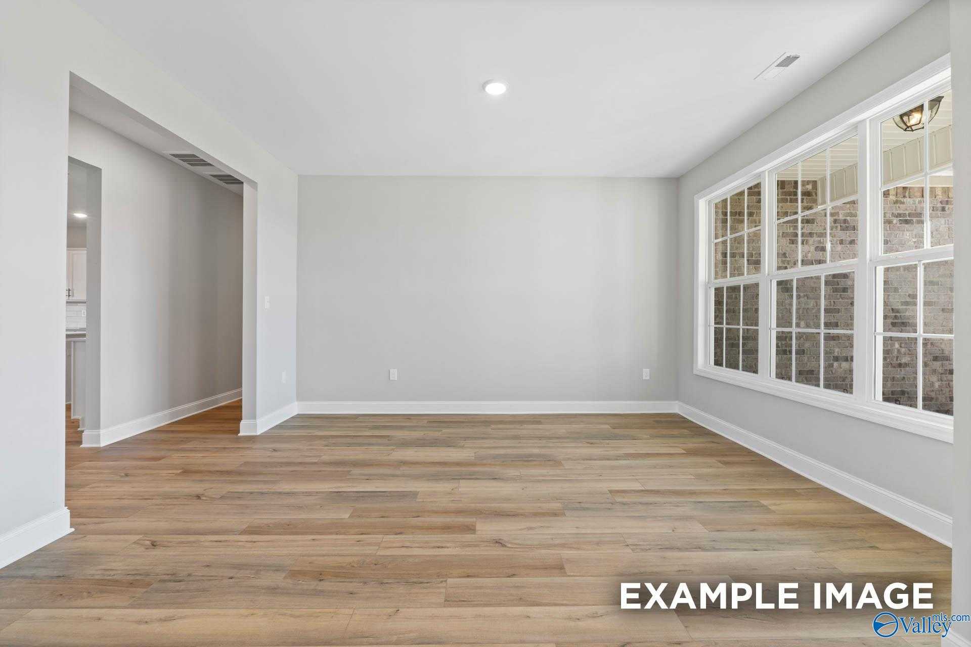 Spacious empty living room with hardwood floors, gray walls, and large windows in 4-bedroom Valencia home, Meridianville, AL