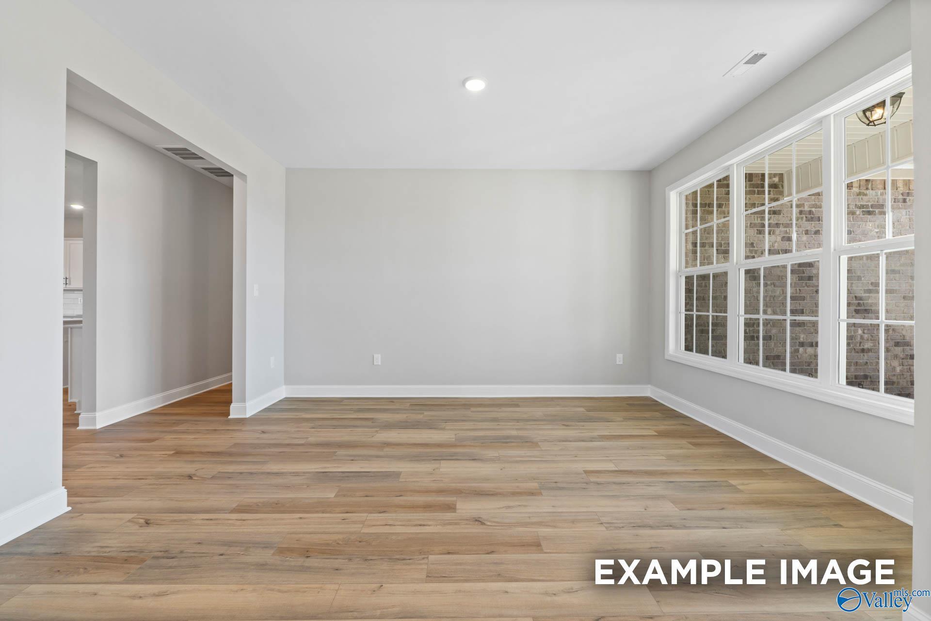 Spacious empty living room with warm hardwood floors, light gray walls, and large brick-view windows in Davidson Homes The Valencia, Toney, Alabama