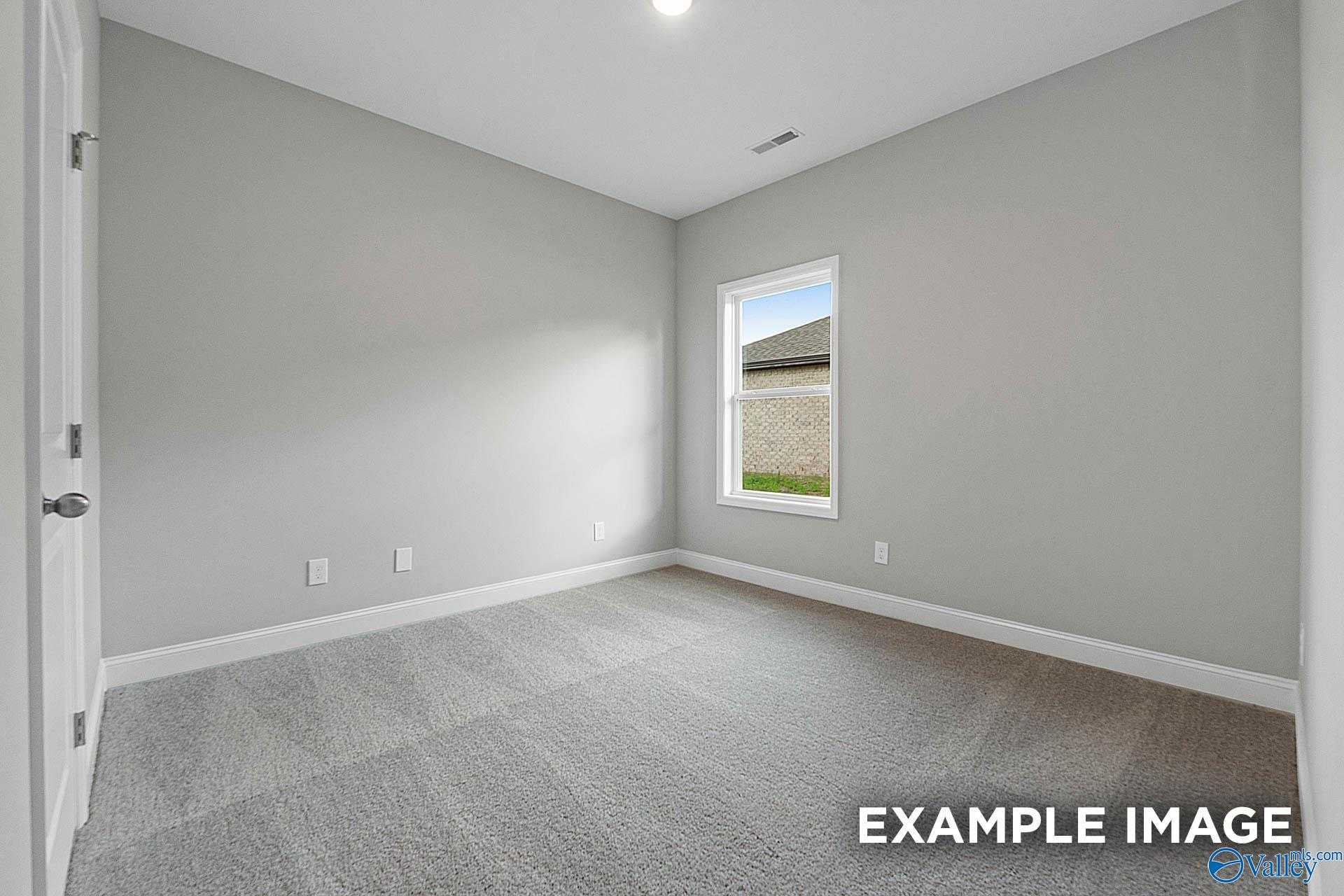 Spacious empty bedroom with gray walls, plush carpet, and window view in Davidson Homes The Franklin E, Hazel Green, AL