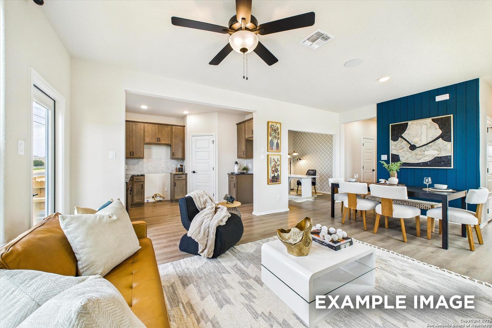 Open-concept living-dining-kitchen with mustard sofa, ceiling fan, and blue accent wall in Davidson Homes The Florence C, San Antonio