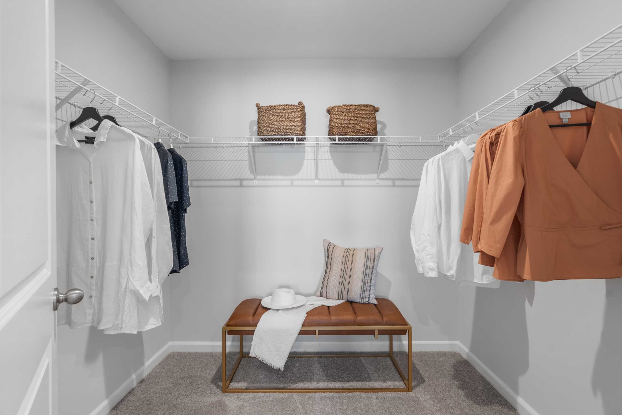 Spacious walk-in closet with wire shelving, hanging clothes, built-in bench, hat and baskets at Stegall Village in Emerson, Georgia