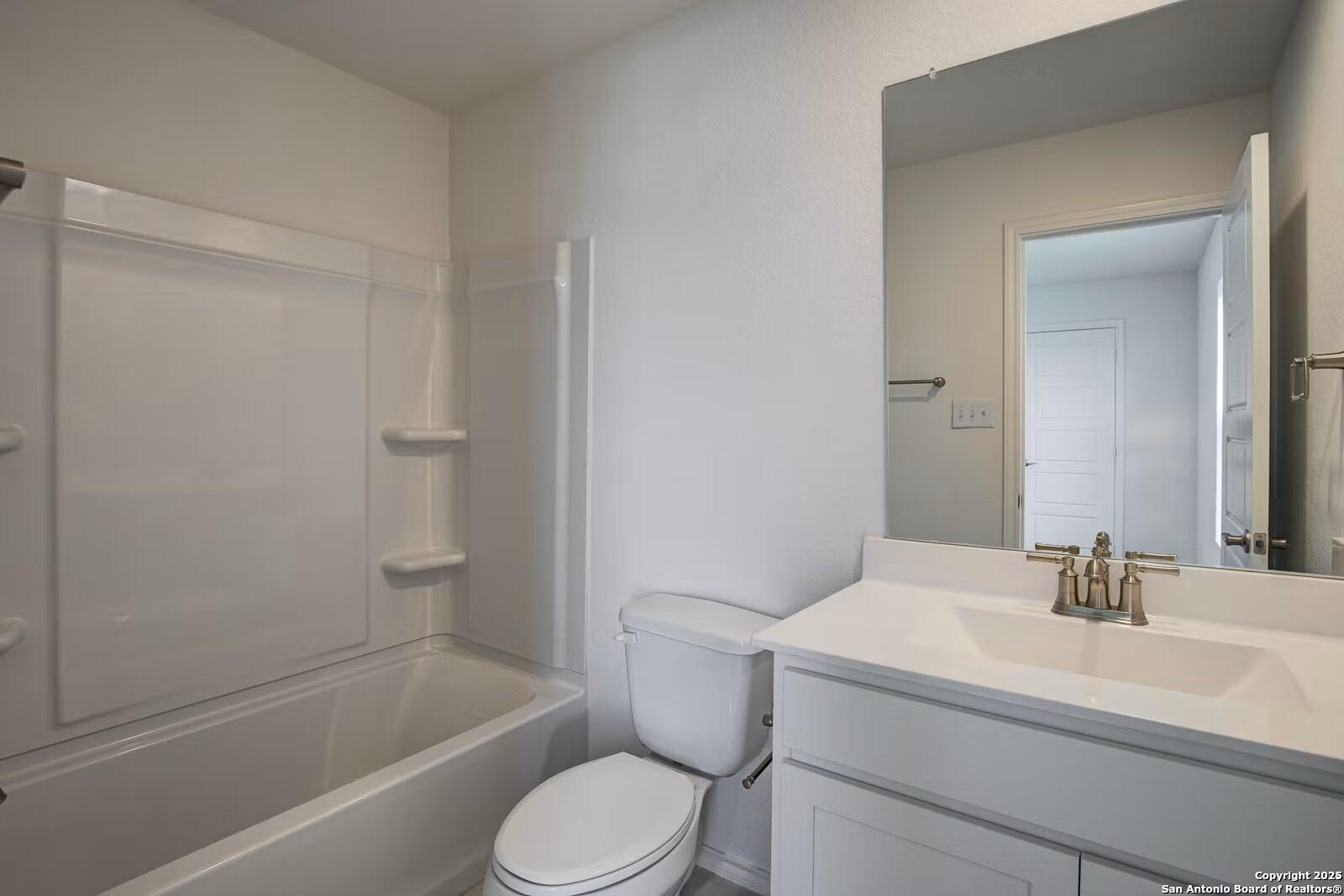 Bright guest bathroom with white tub-shower combo, vanity sink, and large mirror in Davidson Homes The Douglas B, Seguin, Texas