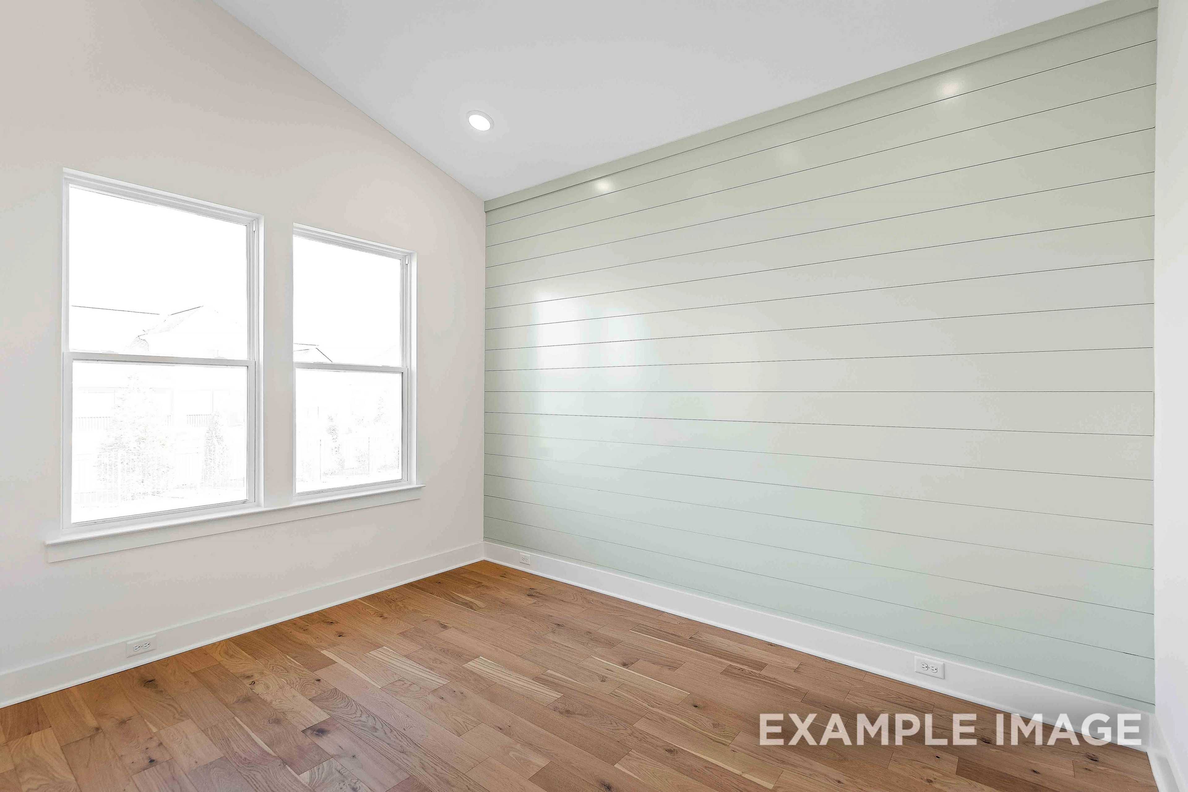 Spacious upper-floor bedroom in The Albany A with light green shiplap wall, hardwood floors, and large double windows