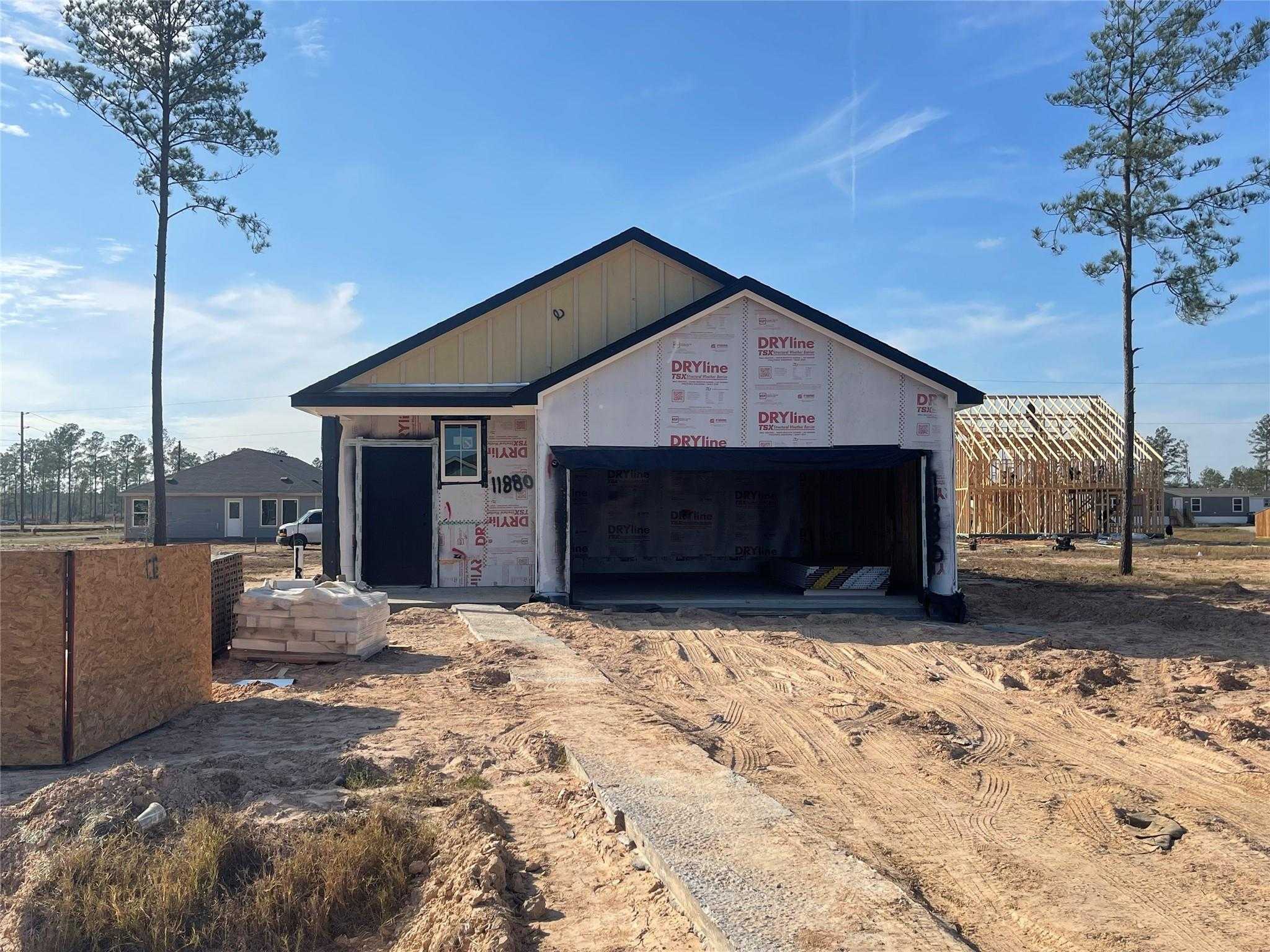 New construction 3-bed, 2-bath home exterior with open 2-car garage, Tyvek wrap, and pine trees in Spring Branch Crossing, Conroe, Texas