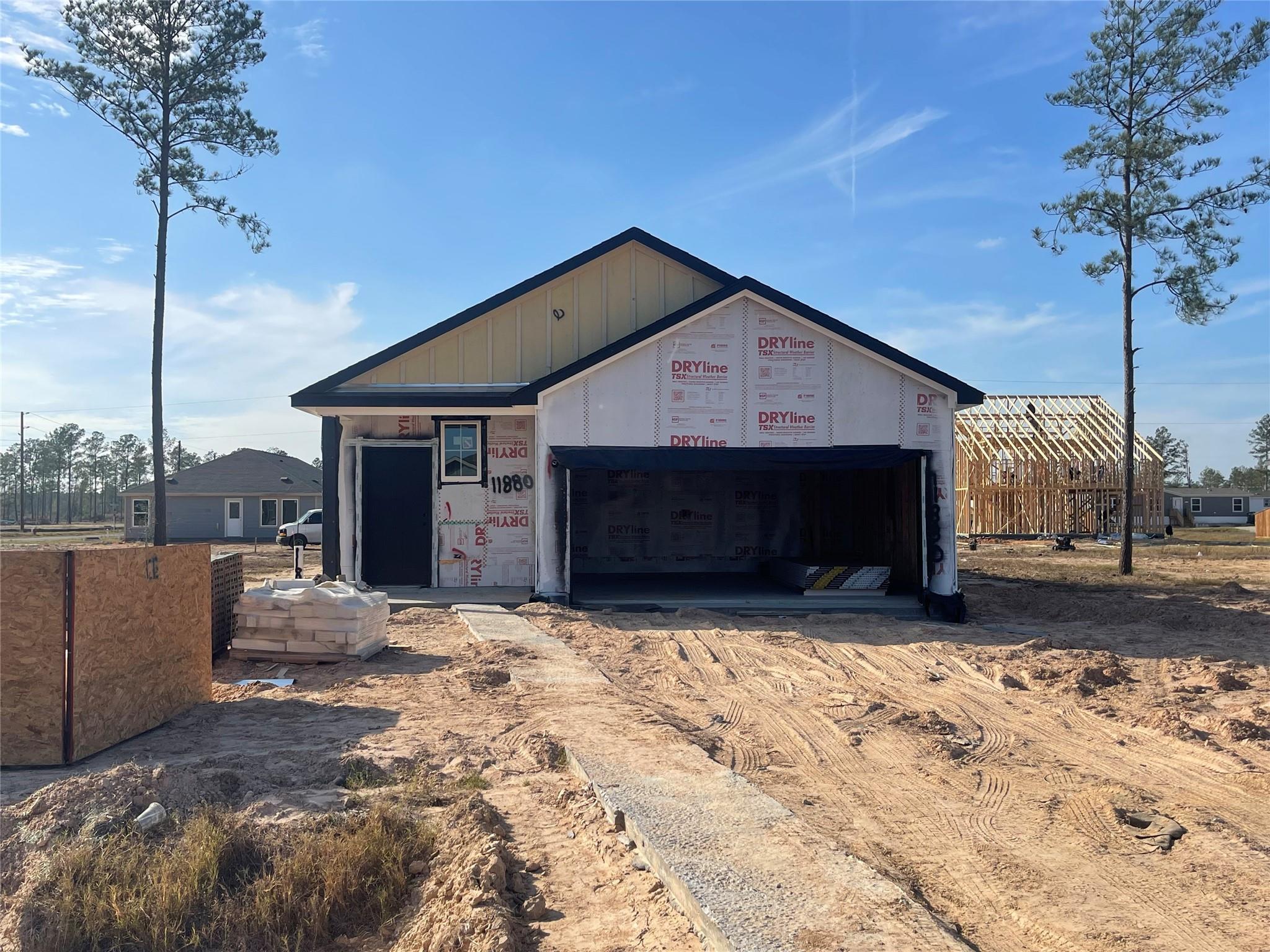 New construction 3-bed, 2-bath home exterior with open 2-car garage, Tyvek wrap, and pine trees in Spring Branch Crossing, Conroe, Texas