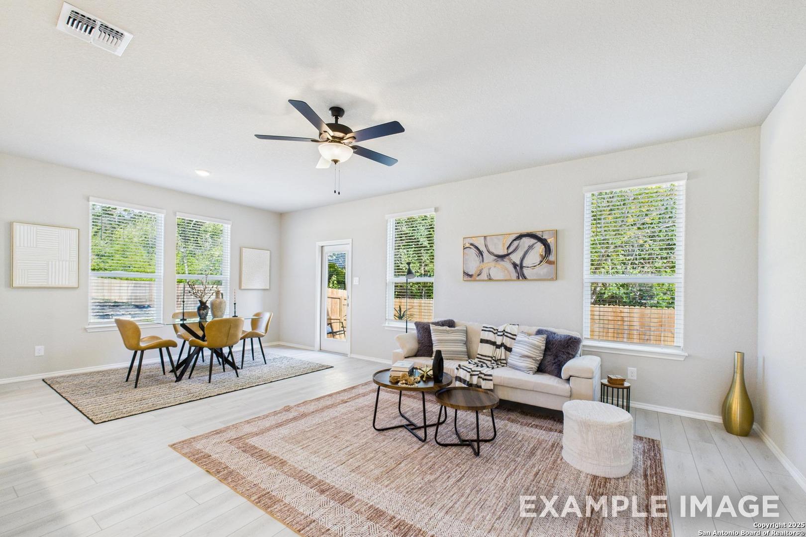 Bright open living and dining area with beige sofa, wood table, ceiling fan, large windows in Davidson Homes The Charlotte B, San Antonio