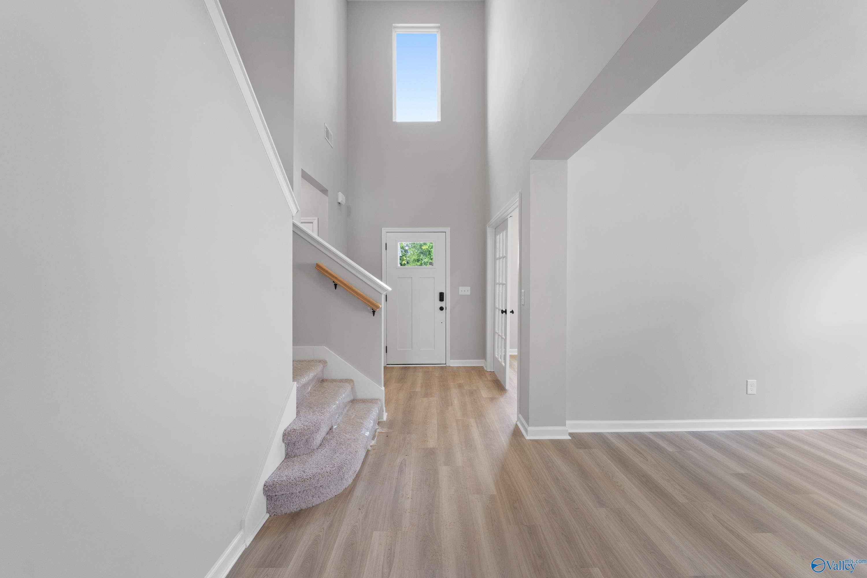 Bright two-story foyer with sweeping white staircase, tall clerestory window, gray walls, and light hardwood floors in Davidson Homes The Dorado, Huntsville AL