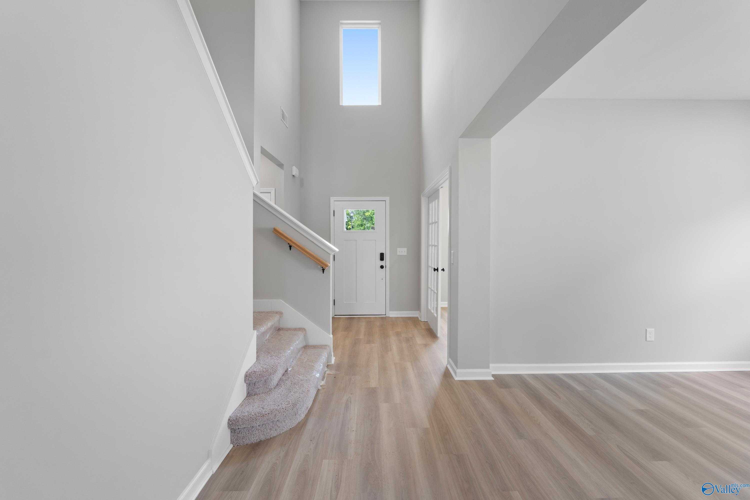 Bright two-story foyer with sweeping white staircase, tall clerestory window, gray walls, and light hardwood floors in Davidson Homes The Dorado, Huntsville AL