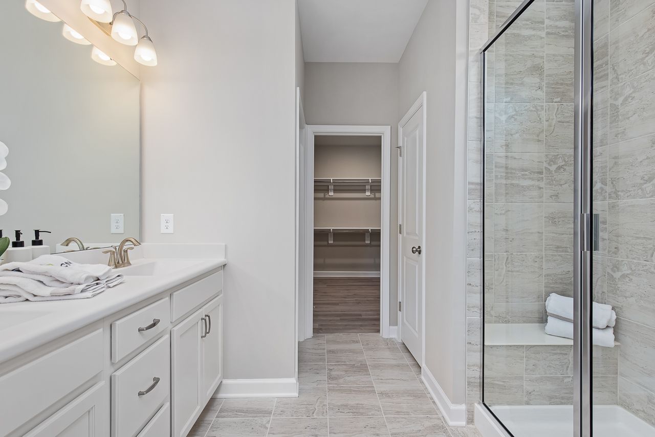 Modern primary bathroom at Woodland Crossing in Zebulon, NC by Davidson Homes featuring a glass shower and walk-in closet.