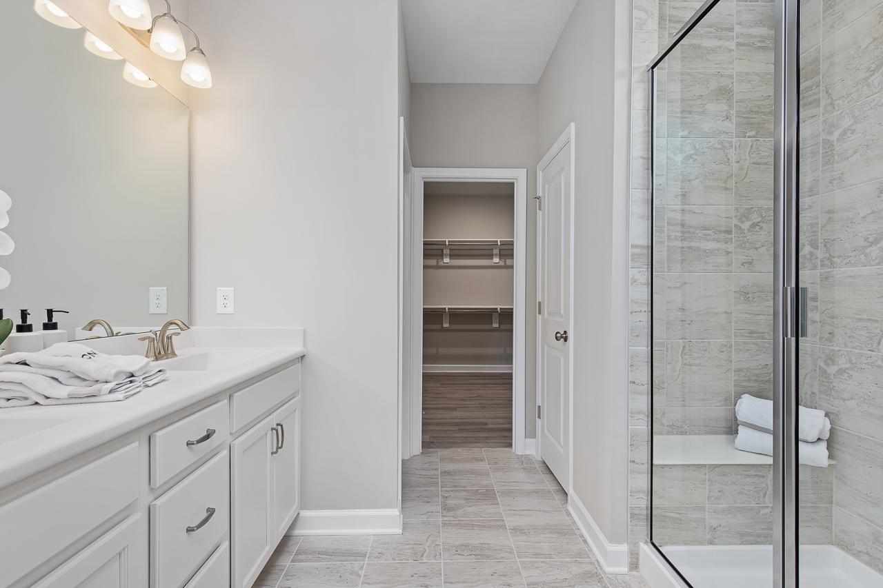 Modern primary bathroom at Woodland Crossing in Zebulon, NC by Davidson Homes featuring a glass shower and walk-in closet.