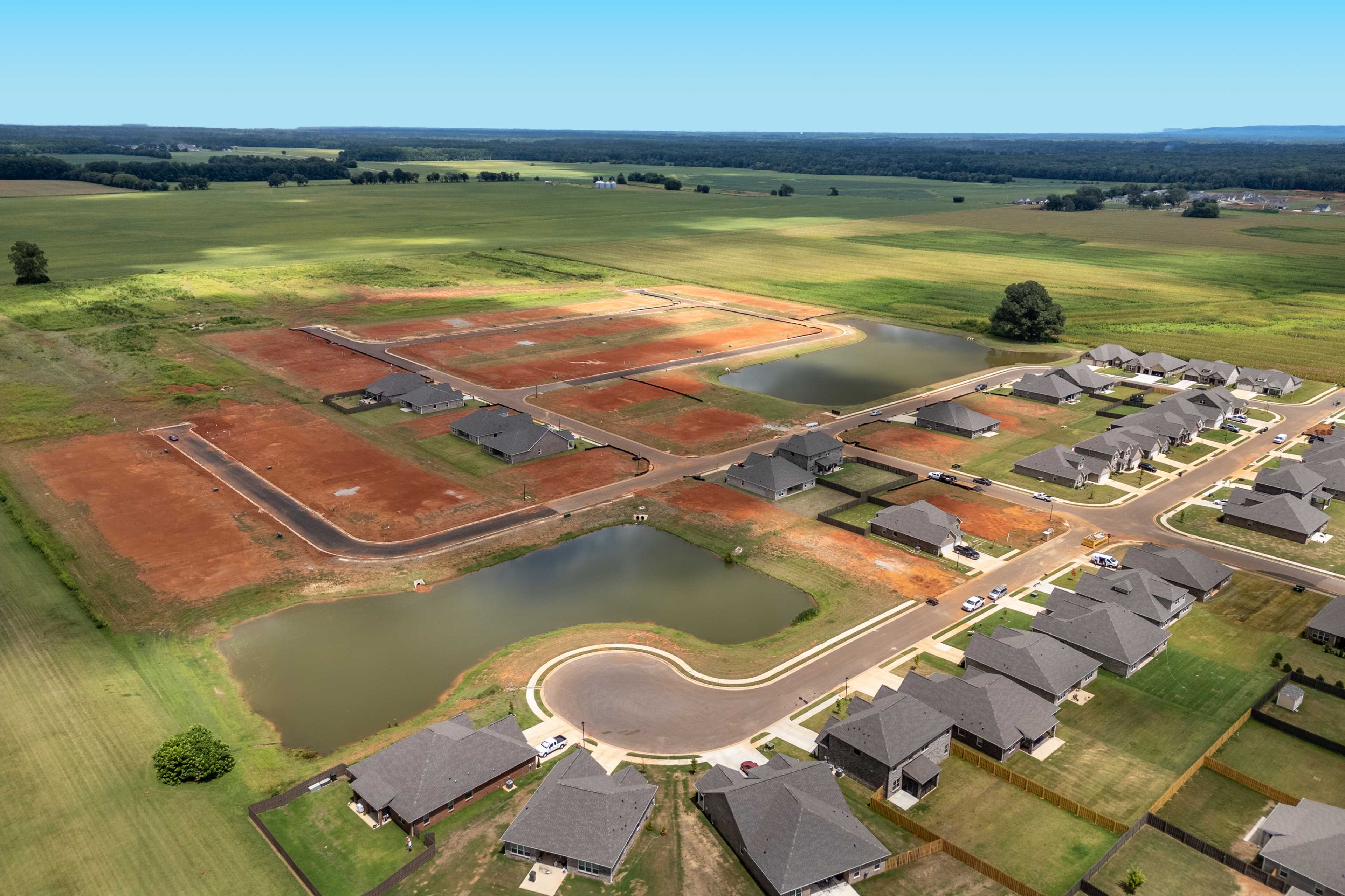 Aerial view of Kendall Downs in Toney Alabama featuring new shingled homes red dirt lots curved ponds and green fields