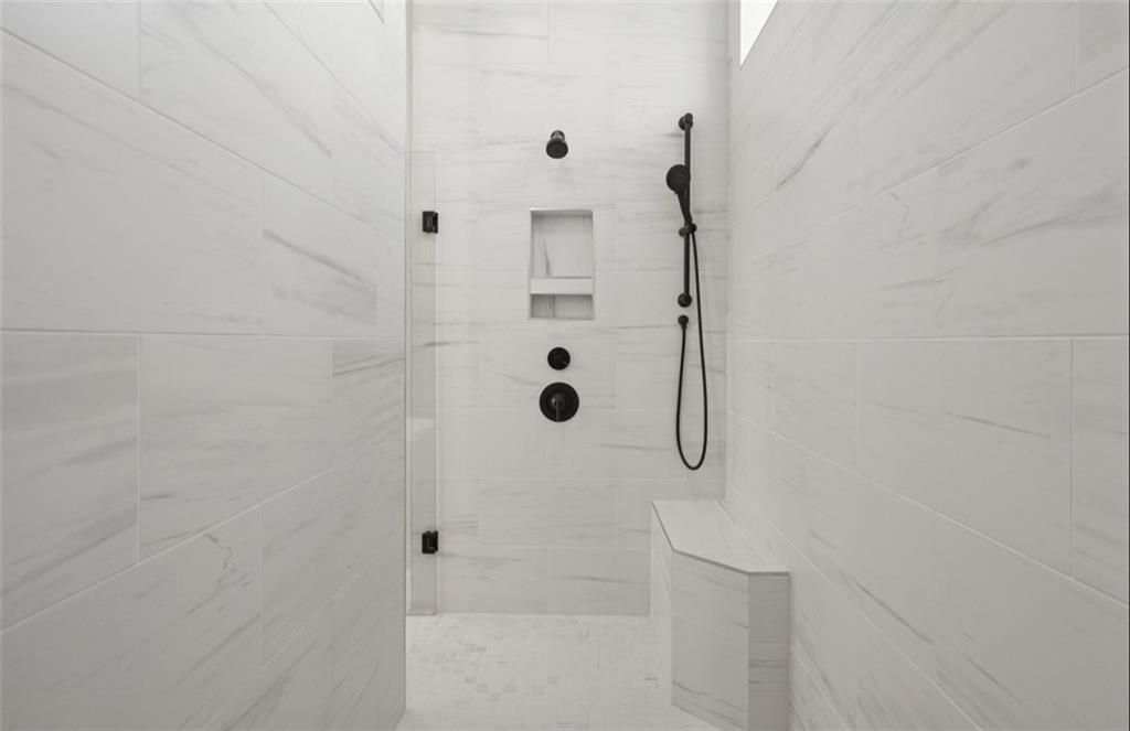 Modern walk-in shower with white subway tiles, black rain showerhead, niche shelves, and bench in Davidson Homes The Seaside A master bath, Woodstock, GA