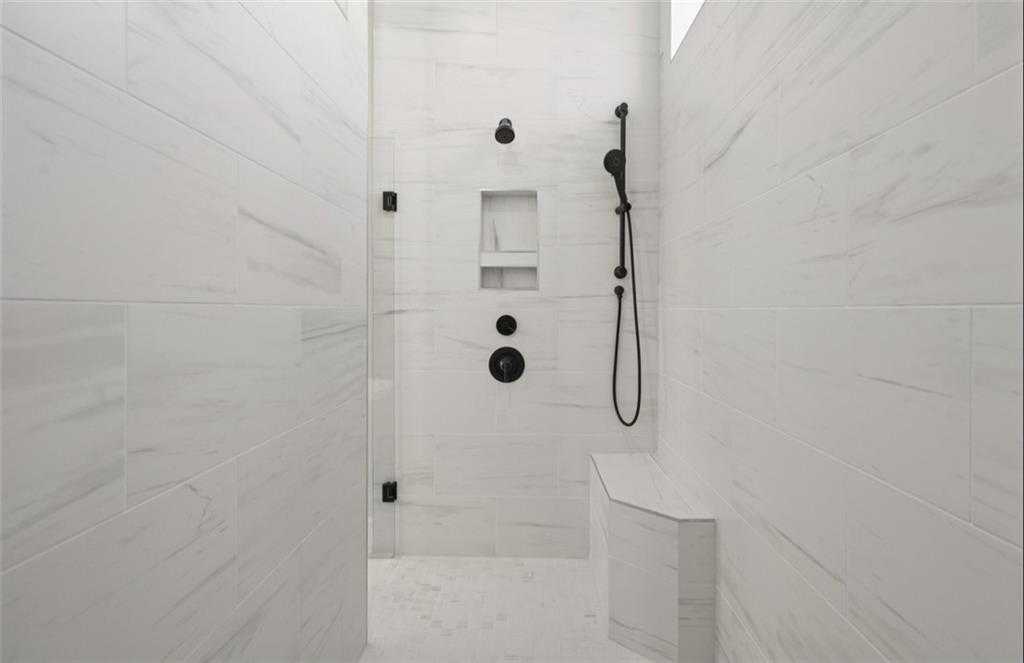 Modern walk-in shower with white subway tiles, black rain showerhead, niche shelves, and bench in Davidson Homes The Seaside A master bath, Woodstock, GA