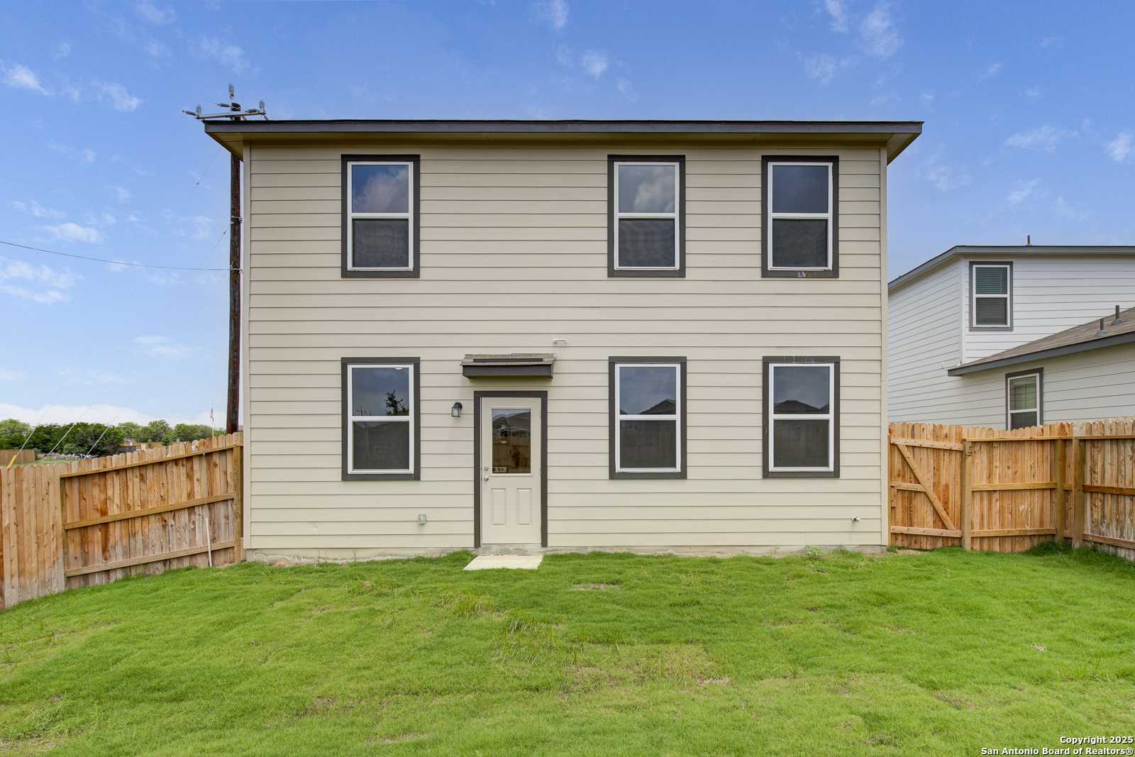 Rear view of two-story Davidson Homes Trinity A with covered patio, fenced backyard, and green lawn in Applewhite Meadows, San Antonio