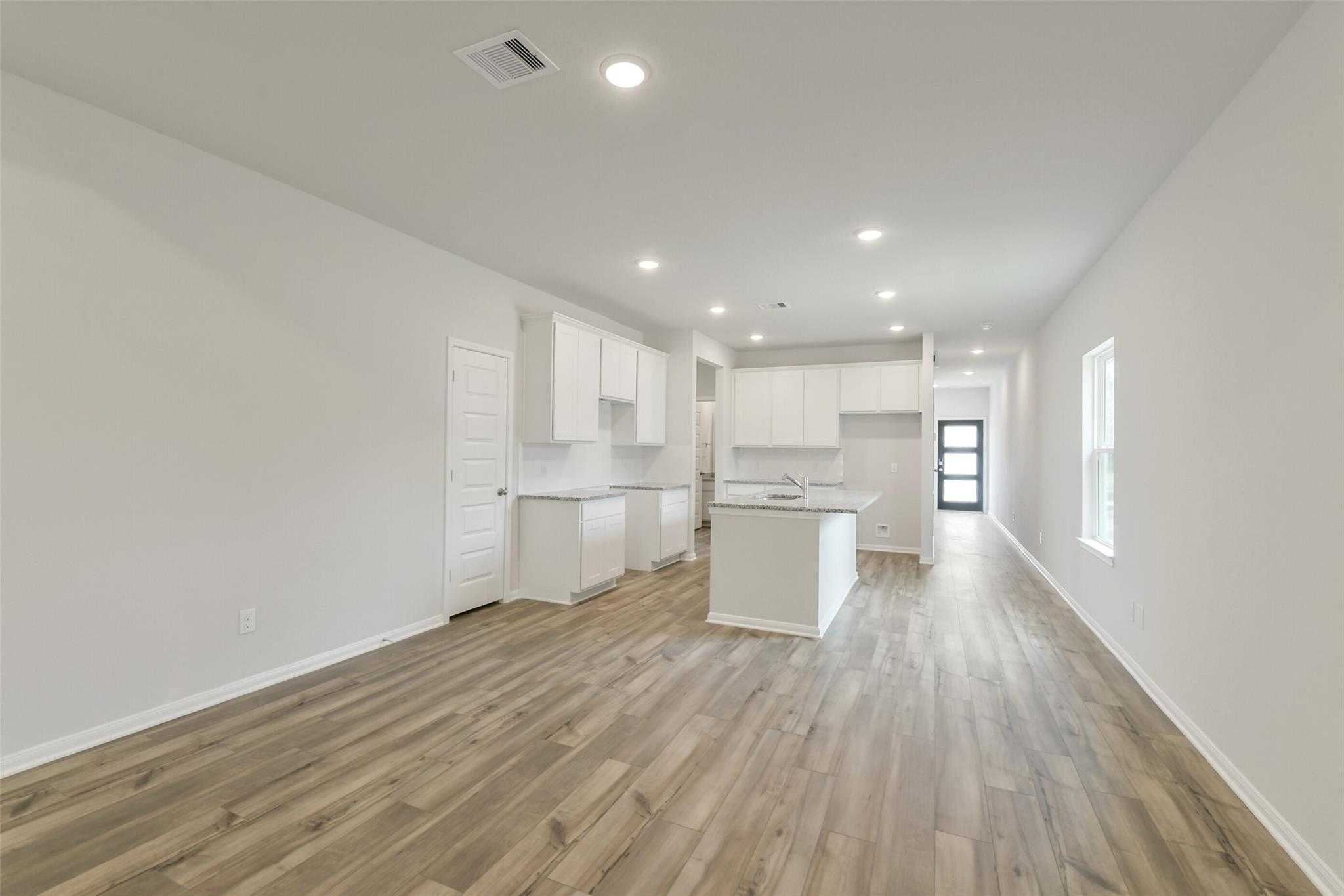 Open-concept kitchen with white cabinets, large island sink, and luxury vinyl plank flooring in Davidson Homes The Frio G, Conroe TX
