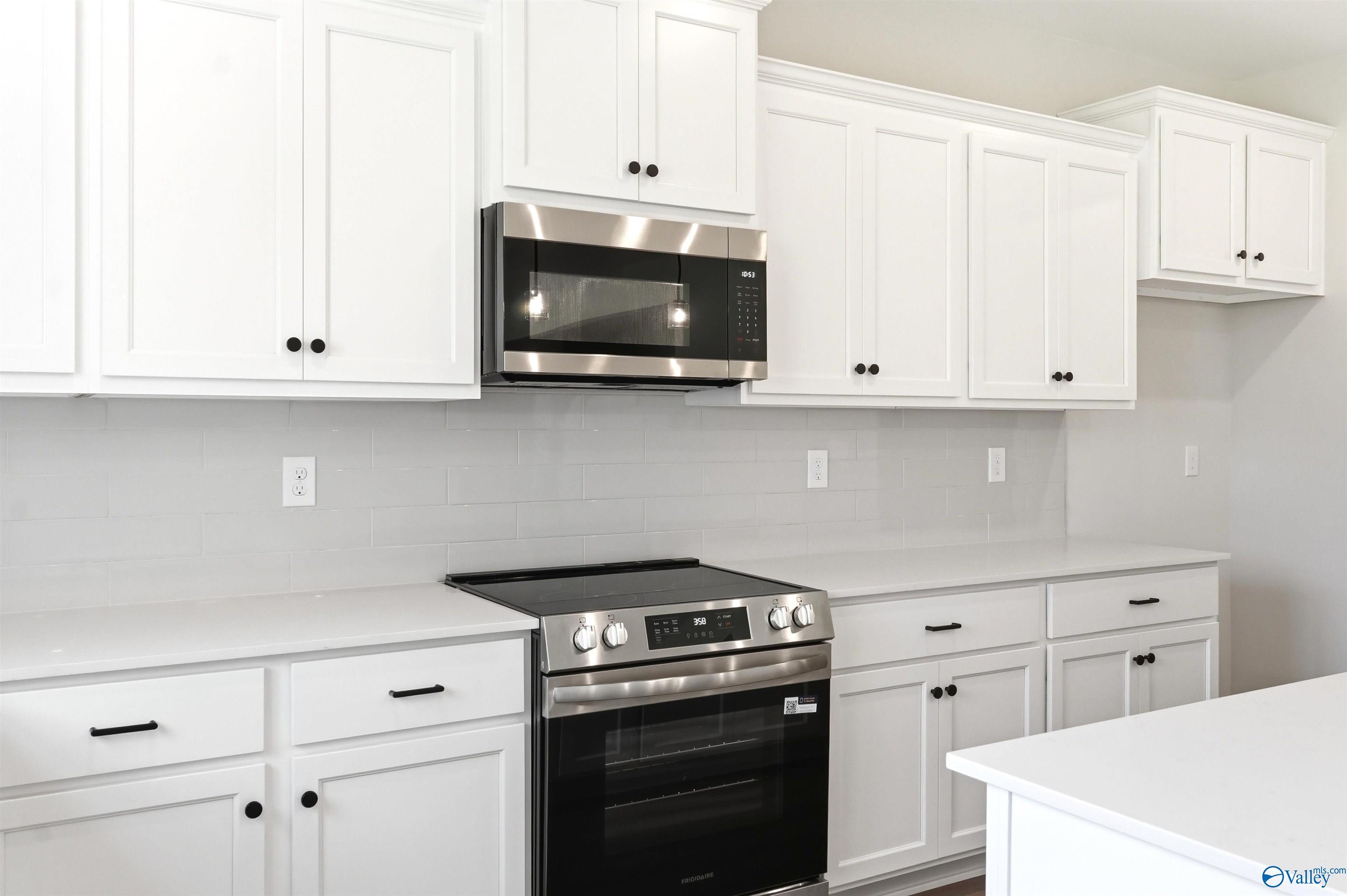 Modern kitchen with white cabinets, quartz countertops, and stainless steel appliances in The Chelsea D, Berry Cove home.