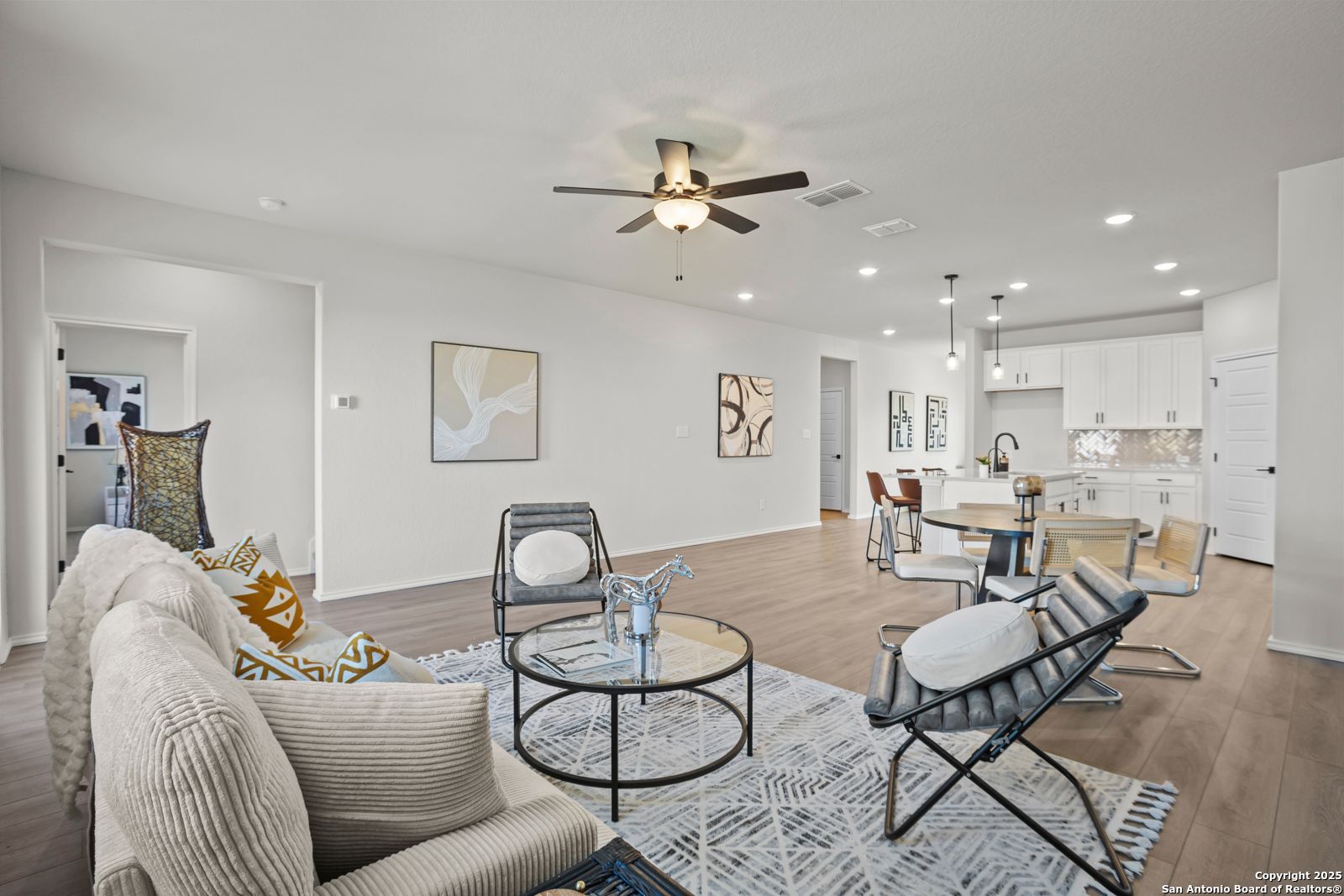 Inviting living room with plush beige sofas, modern chairs, abstract art, and open white kitchen in Davidson Homes The Douglas C, Seguin, Texas