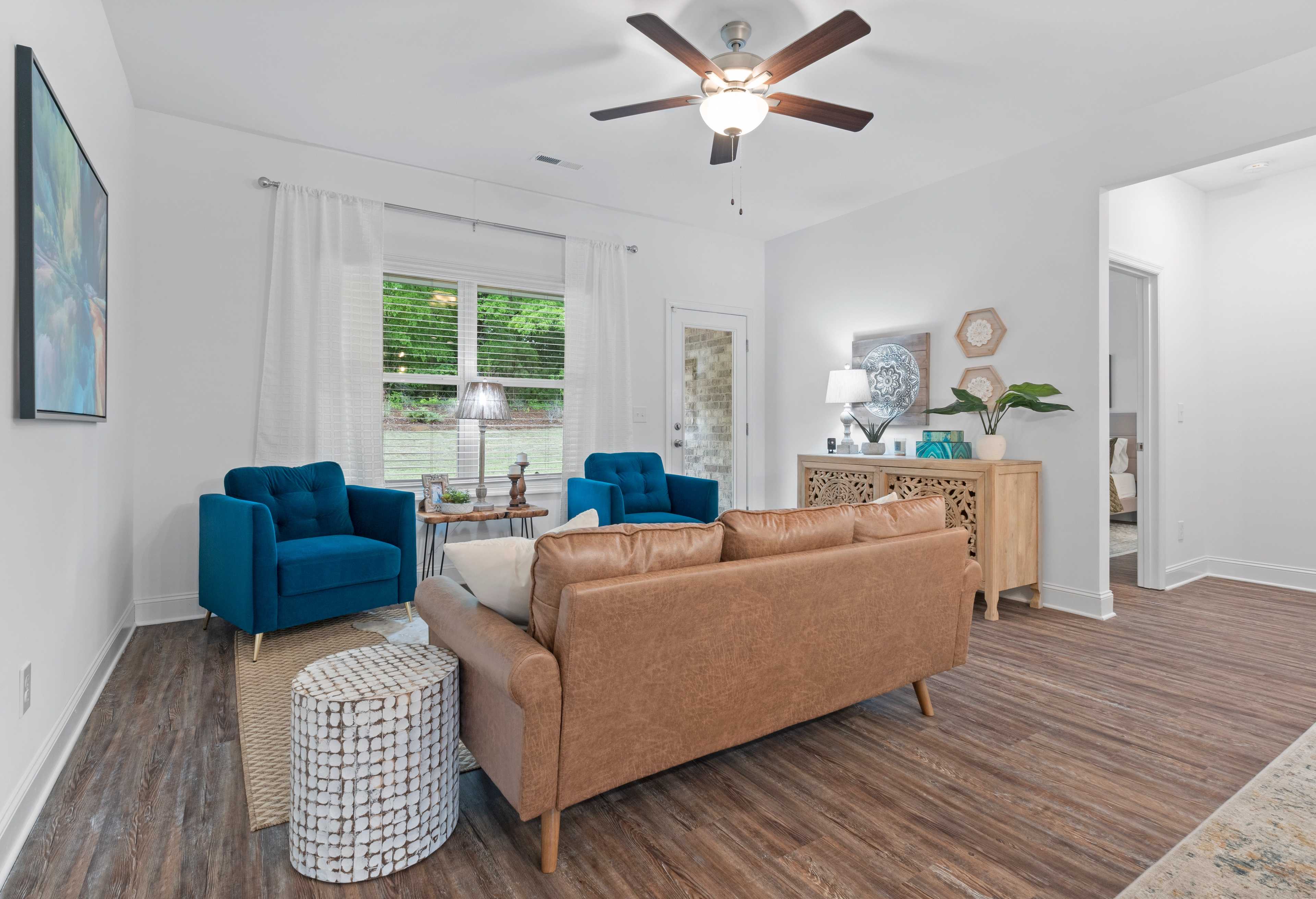 Cozy living room in The Cumberland by Davidson Homes, featuring blue velvet armchairs, tan leather sofa, hardwood floors, and large windows